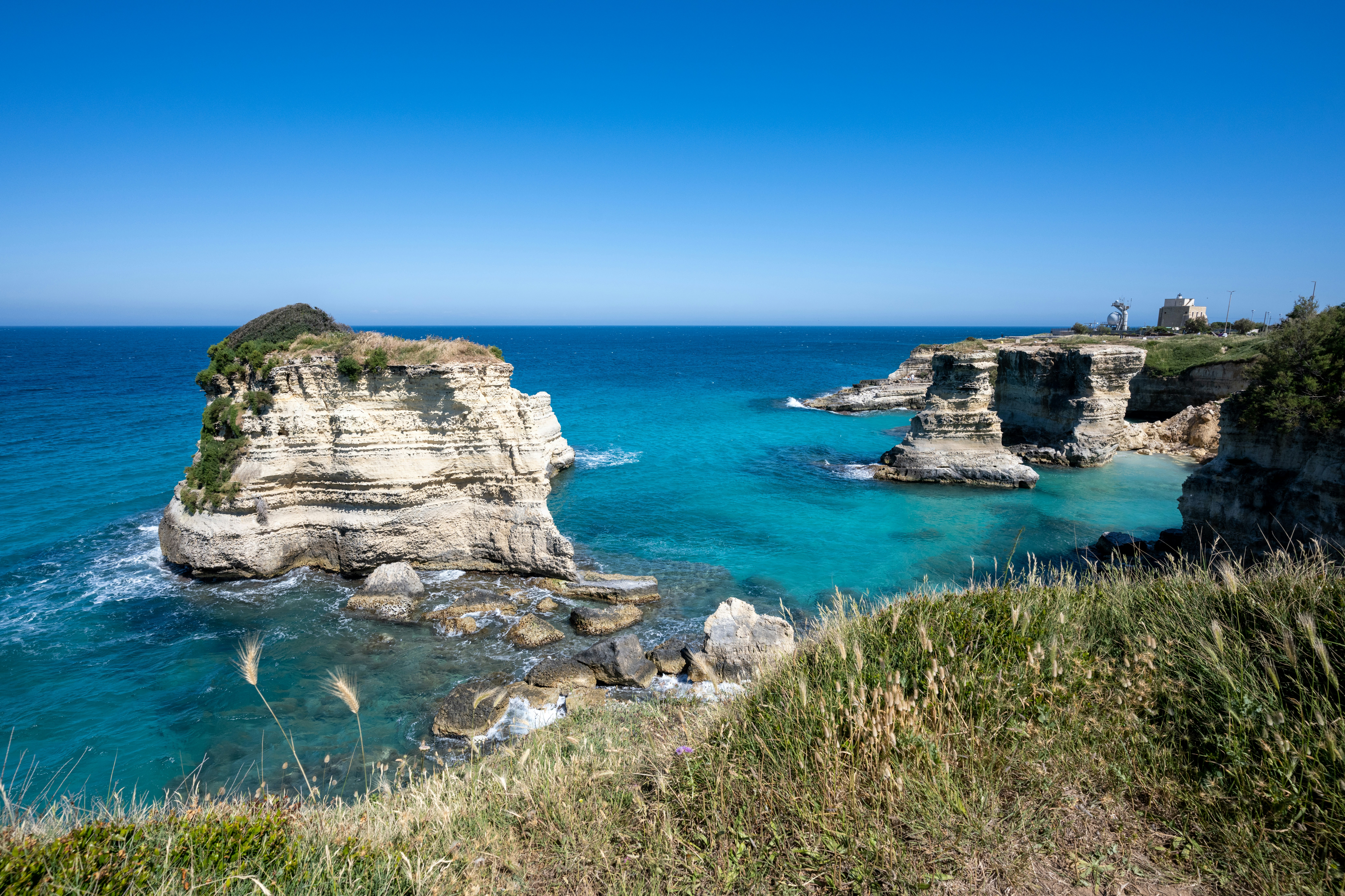 Mare azzurro limpido, scogliere rocciose ed erba verde.