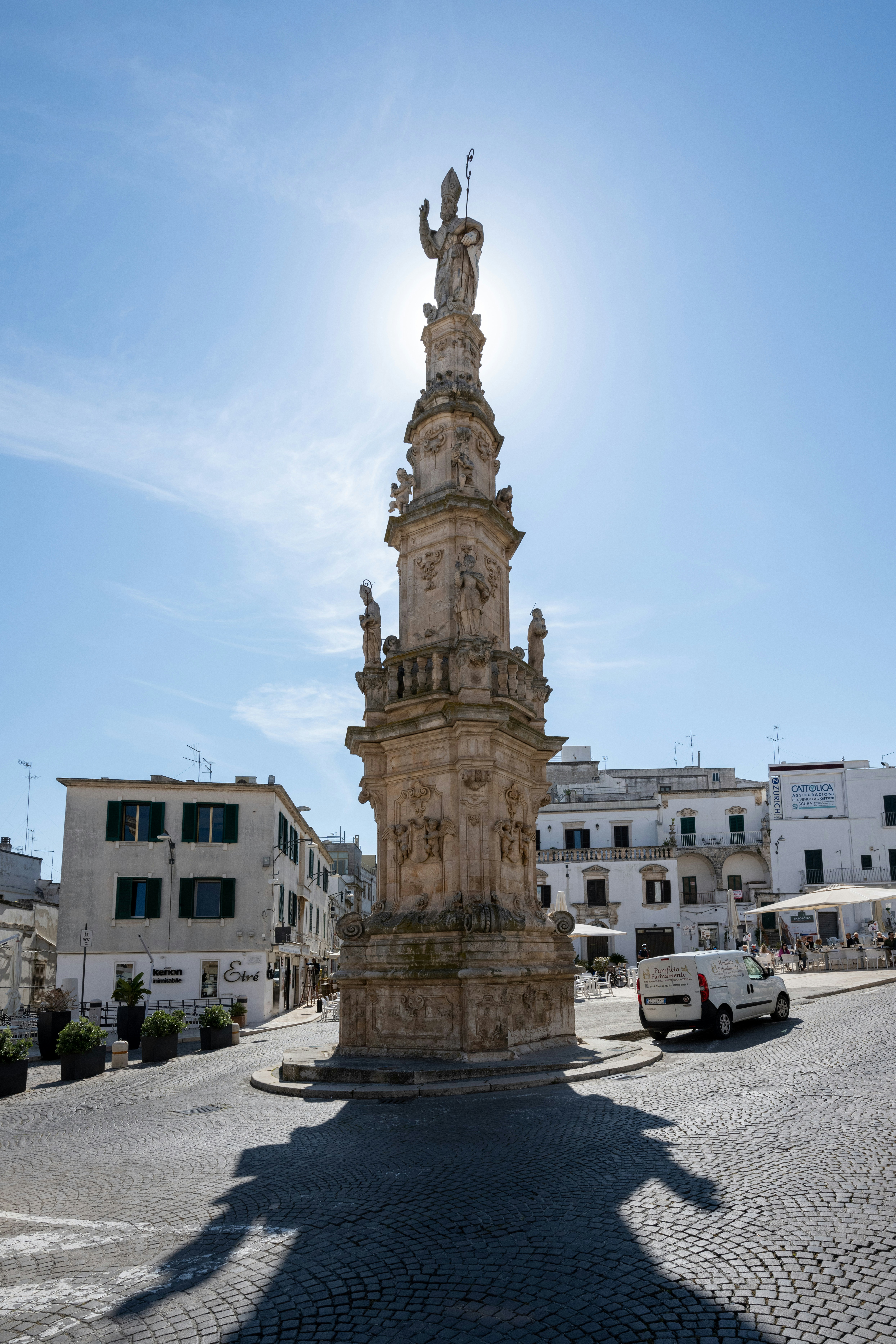 Monumento in pietra ornato stagliato dal sole in una piazza del paese.