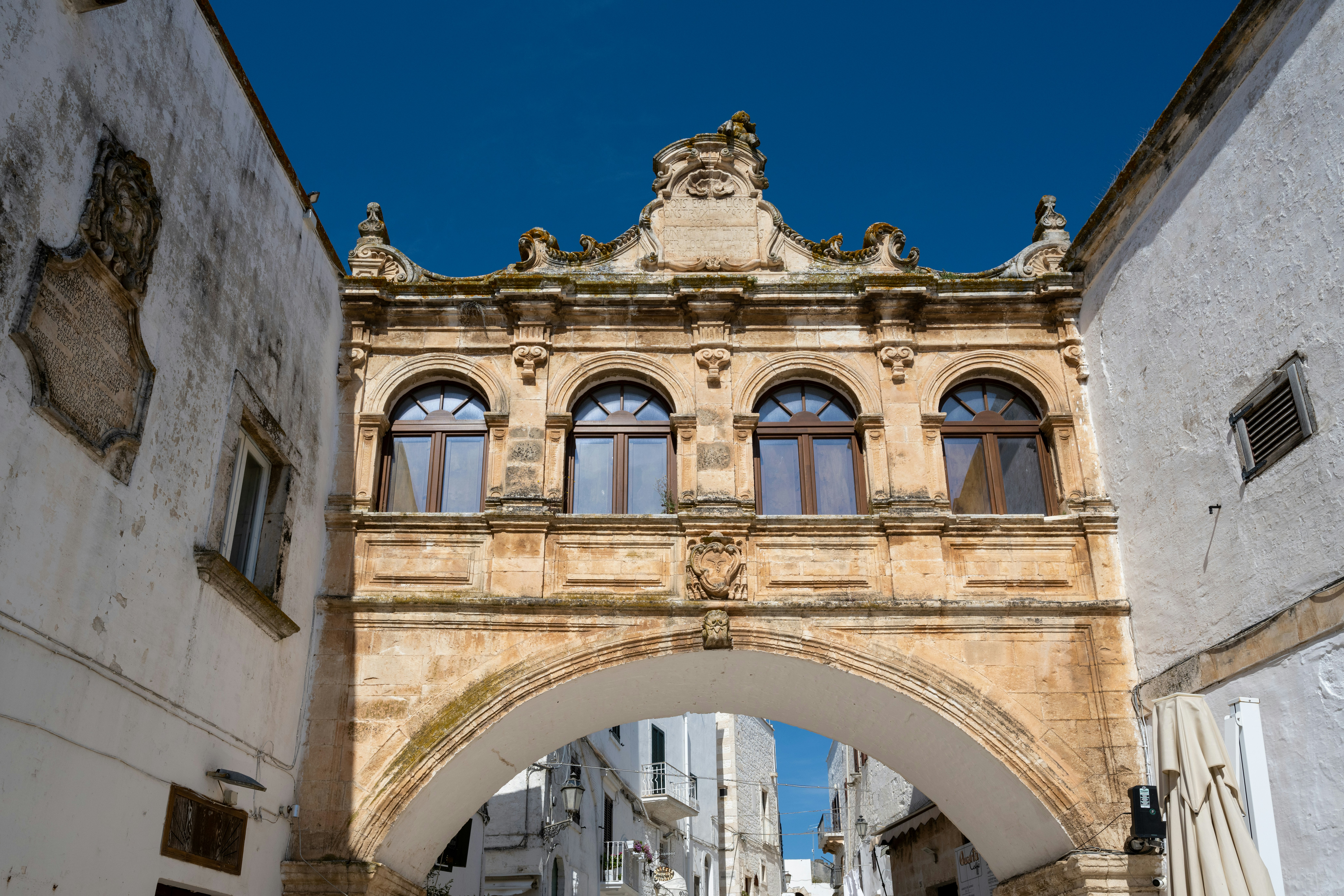 Arco di pietra ornato che collega edifici bianchi sotto un cielo azzurro.