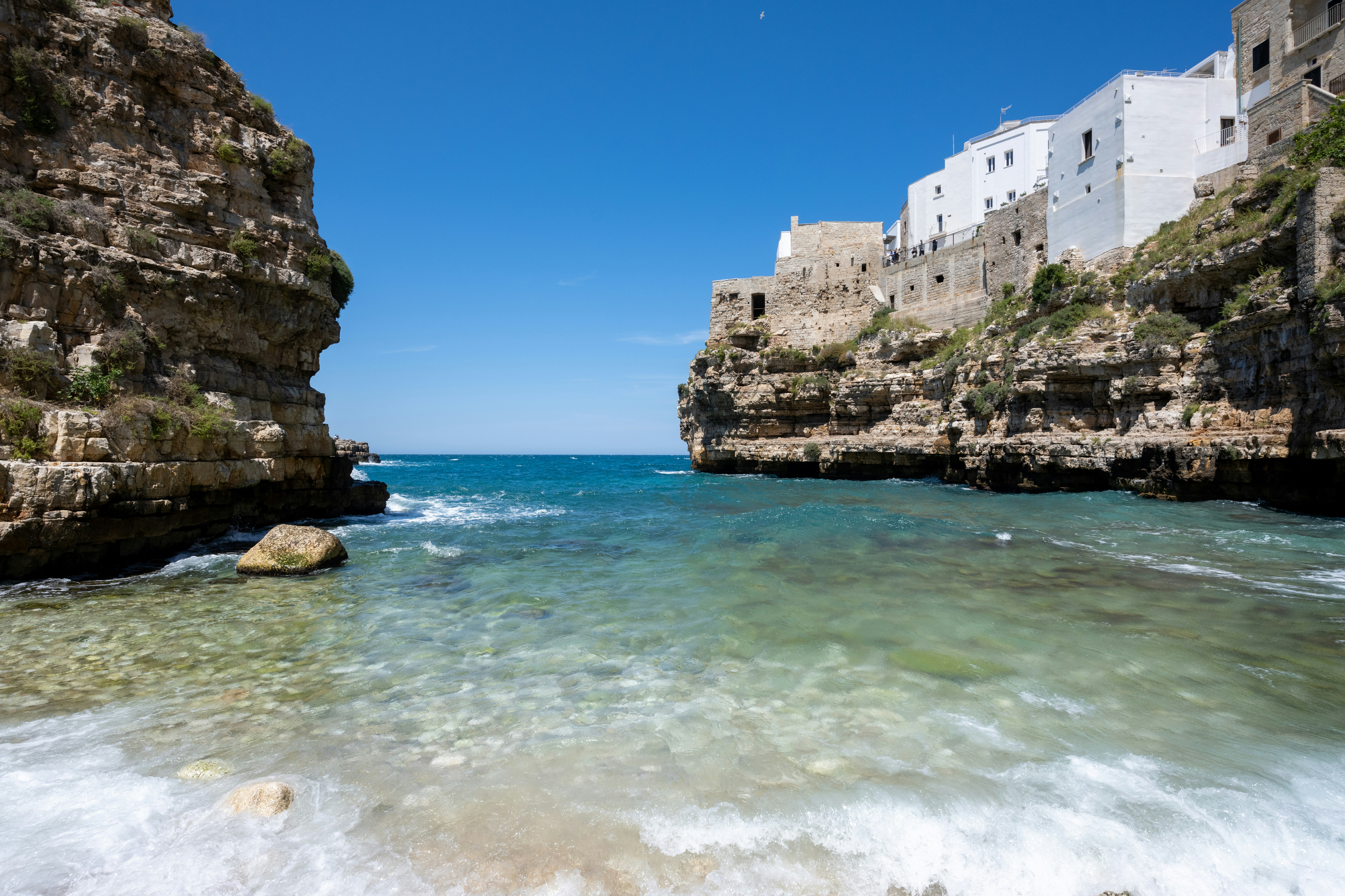 Mare azzurro limpido tra scogliere rocciose e città costiera bianca.