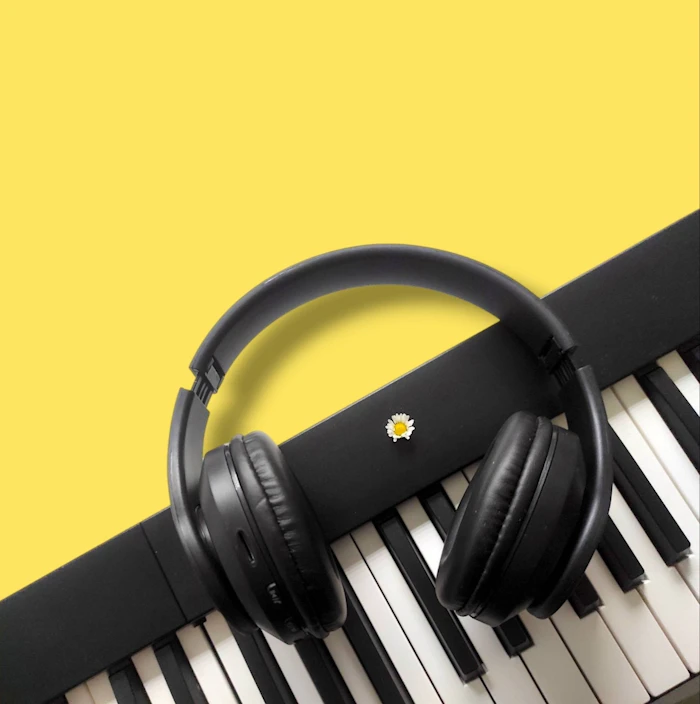 Black over-ear headphones resting on piano keys against yellow