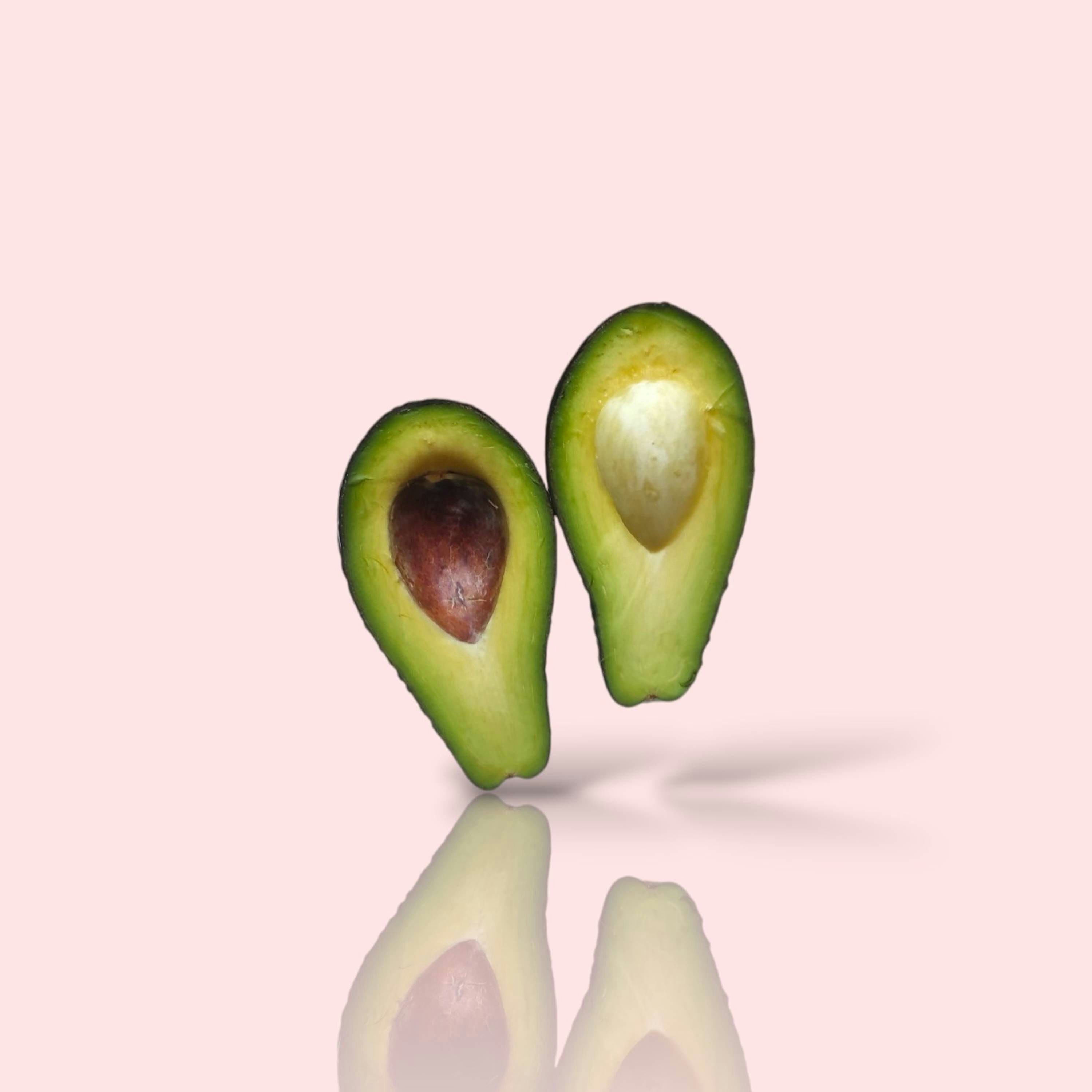 Due metà di avocado che fluttuano sopra una superficie rosa riflettente.
