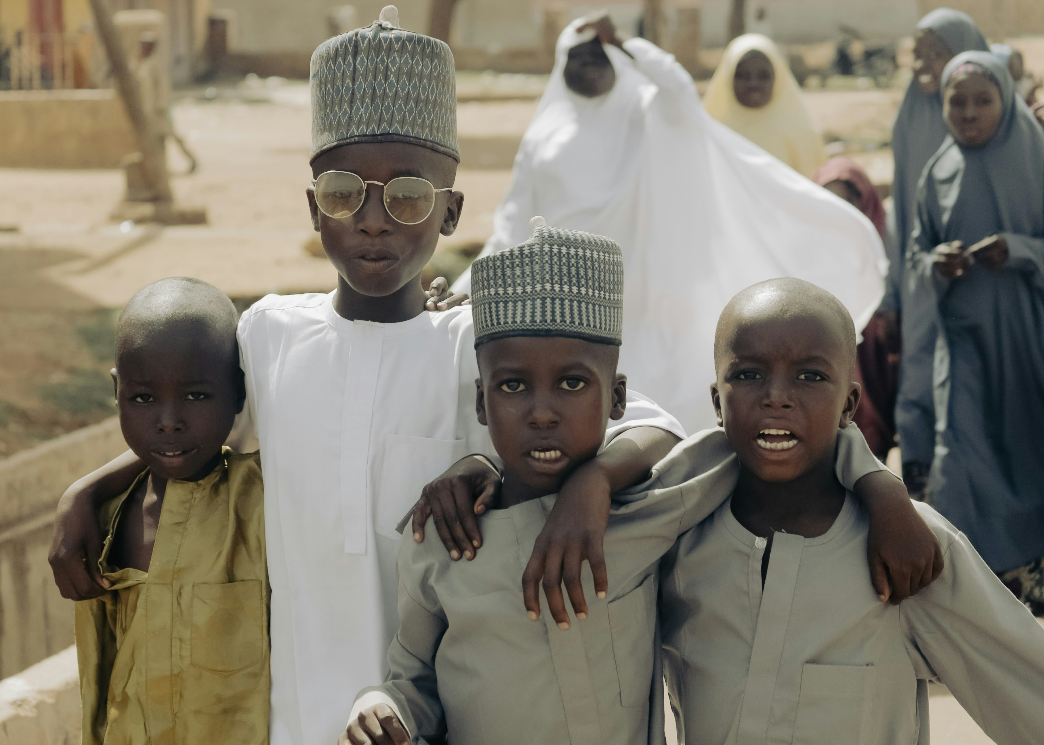 Four young boys in traditional attire stand together outdoors.