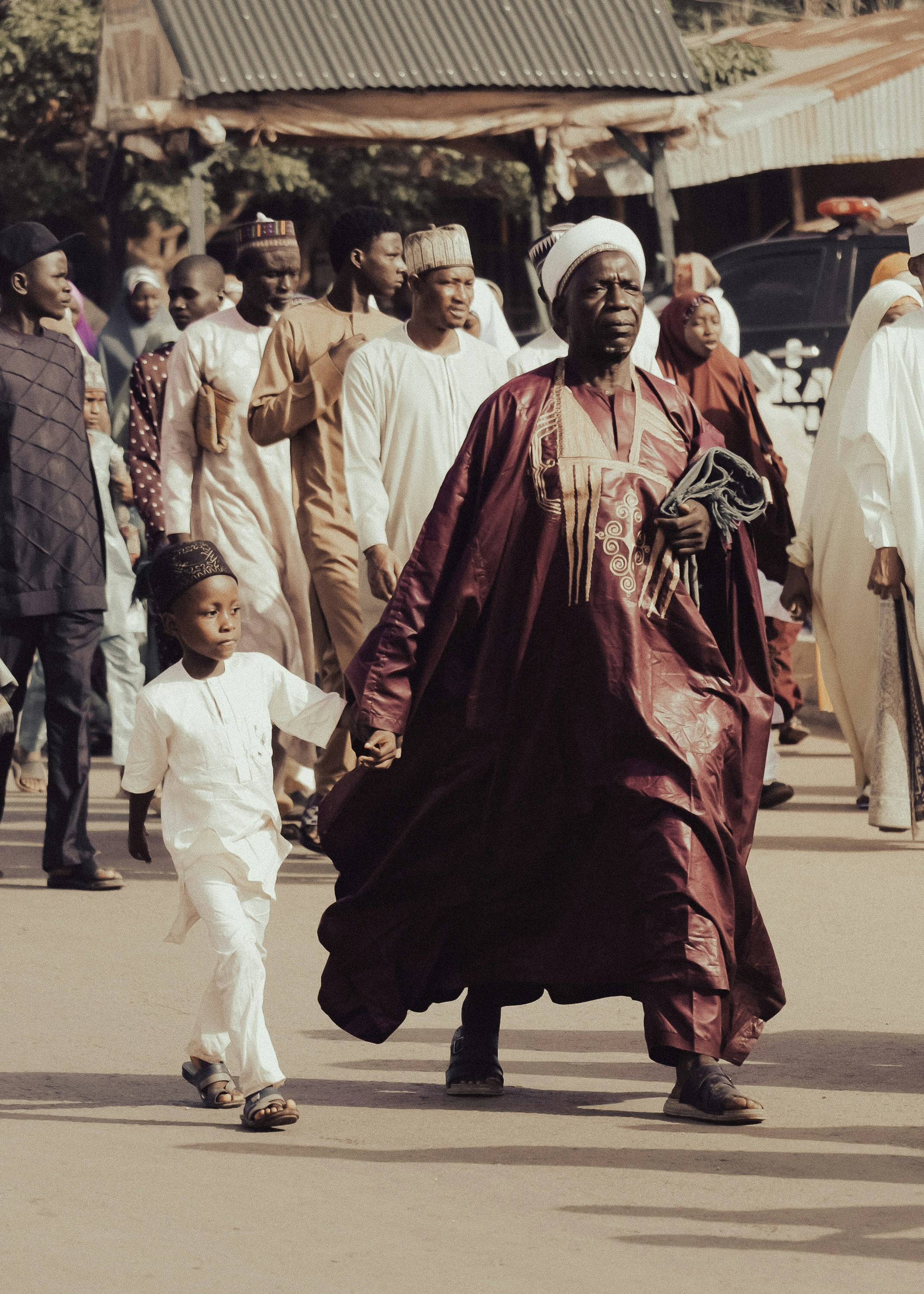 Pria dan anak laki-laki Afrika dengan pakaian tradisional berjalan di jalan.