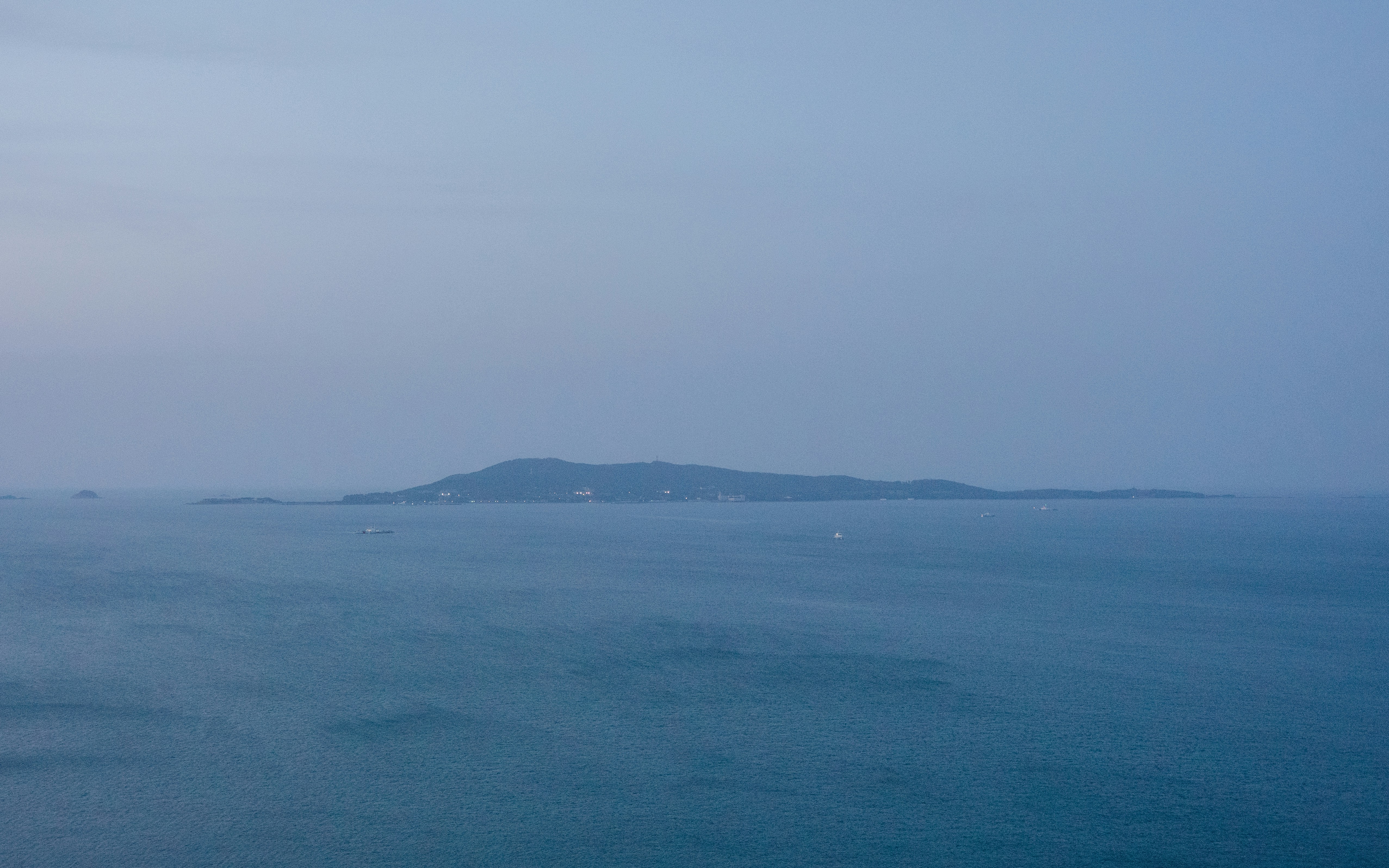 Isola lontana nell'oceano nebbioso sotto un cielo soffuso.