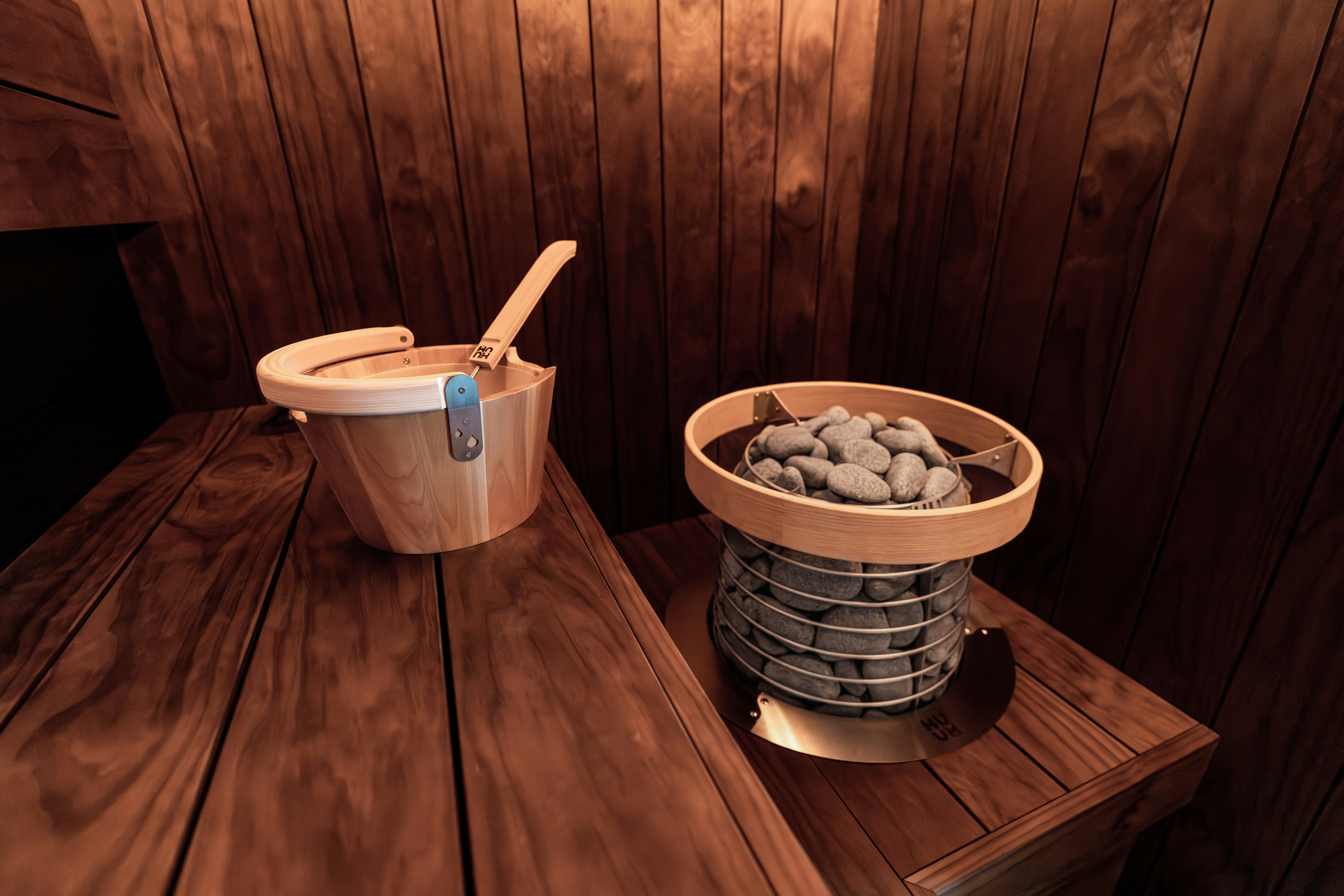 Sauna traditionnel en bois avec seau, louche et chauffage en pierre chaude.