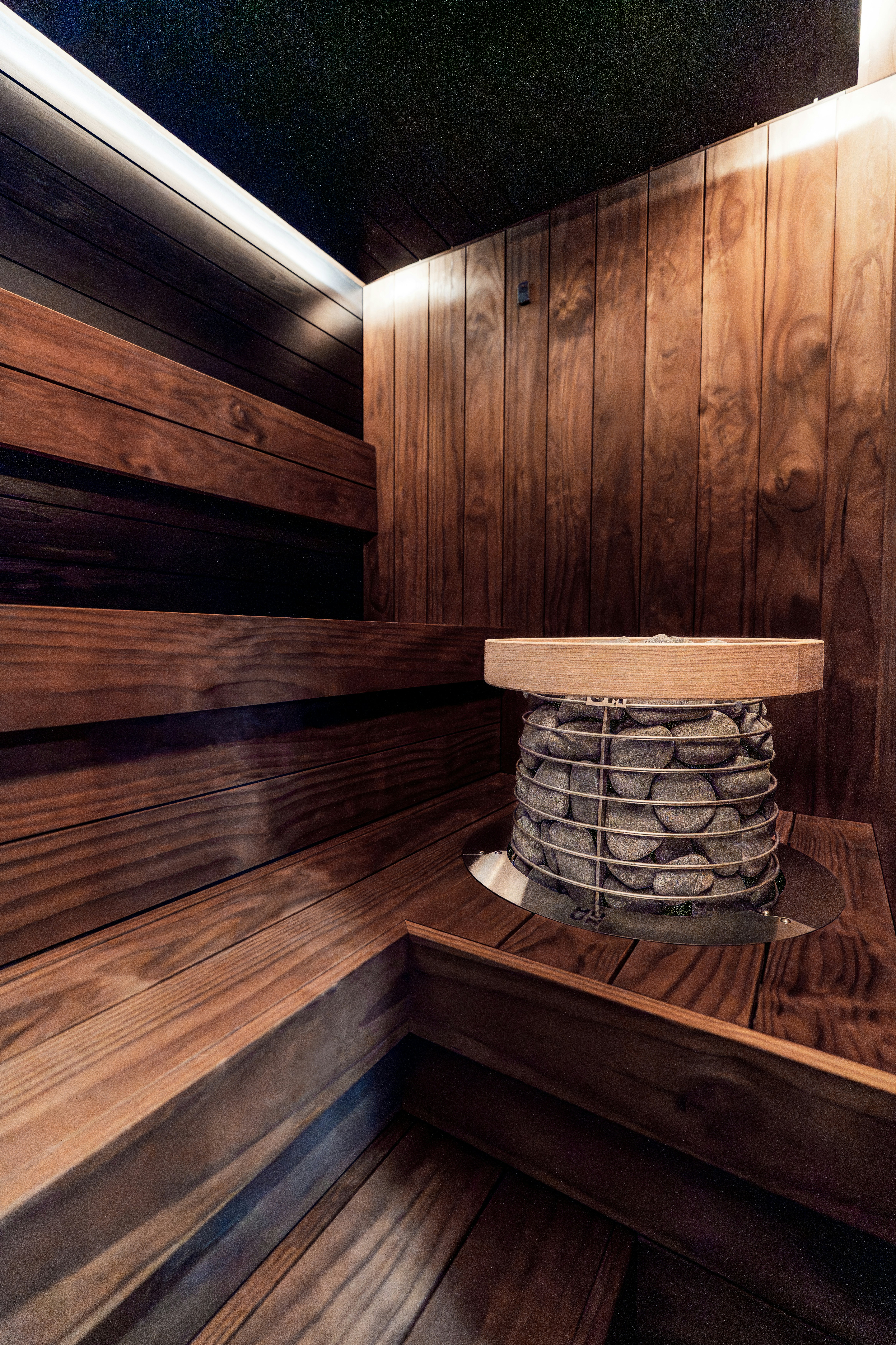 Moderne Holzsauna mit gestuften Bänken und Steinofen.