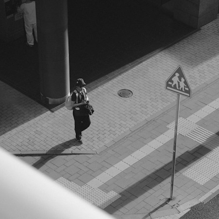 Person walking on a sidewalk near a school crossing sign during the morning school commute