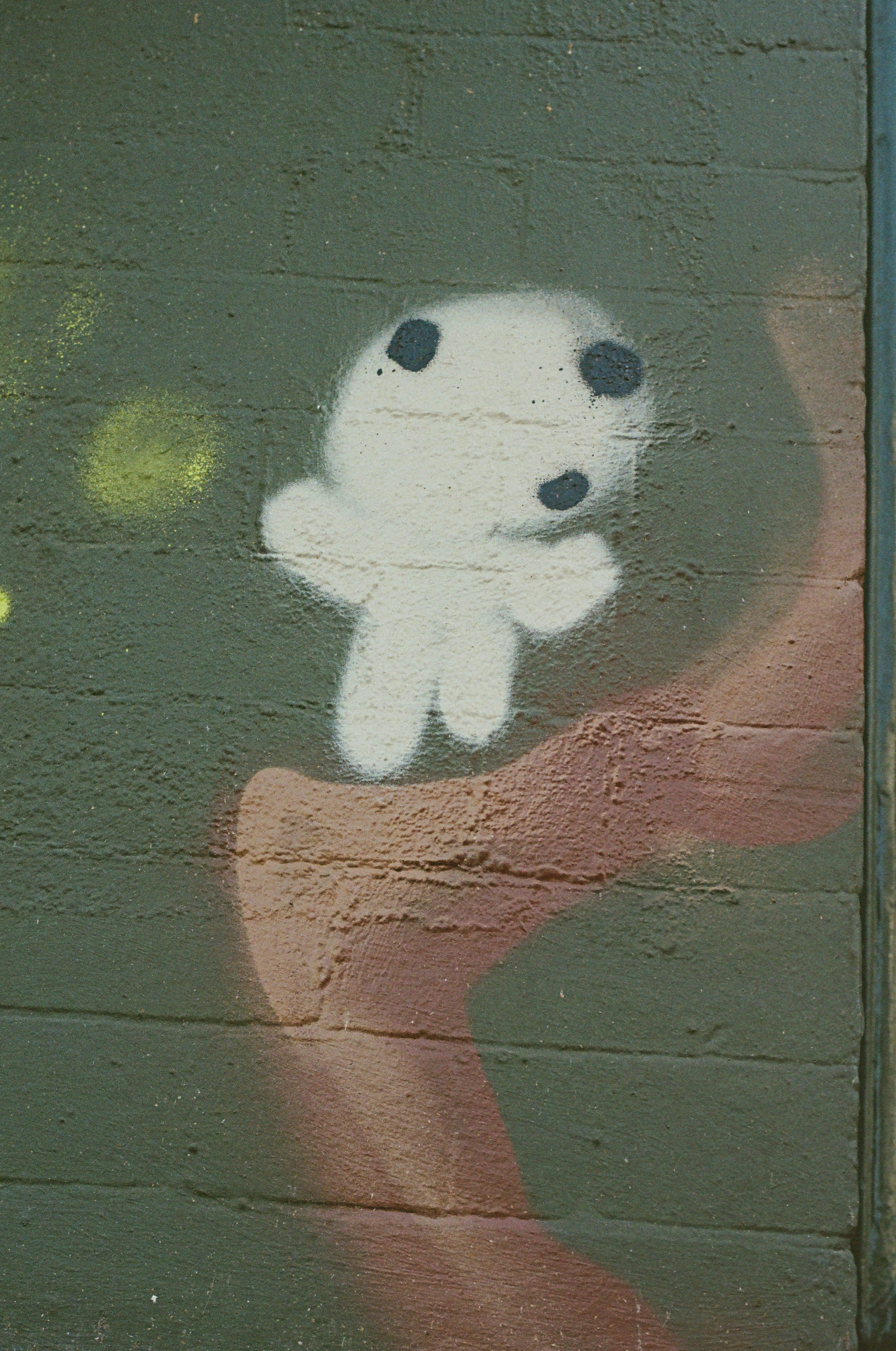 White blob character graffiti on a dark brick wall.