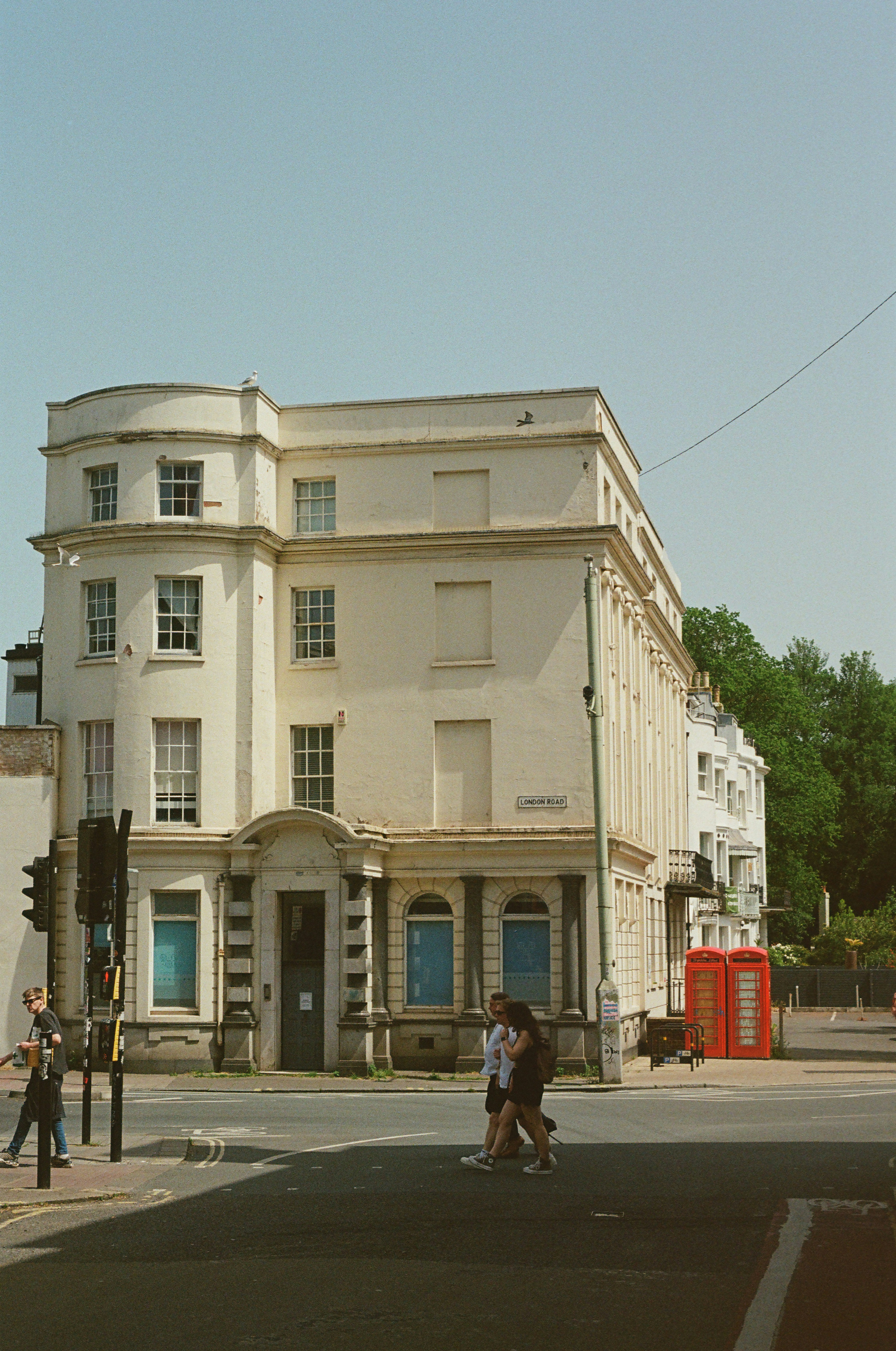 People walk past a large building and red telephone booths.