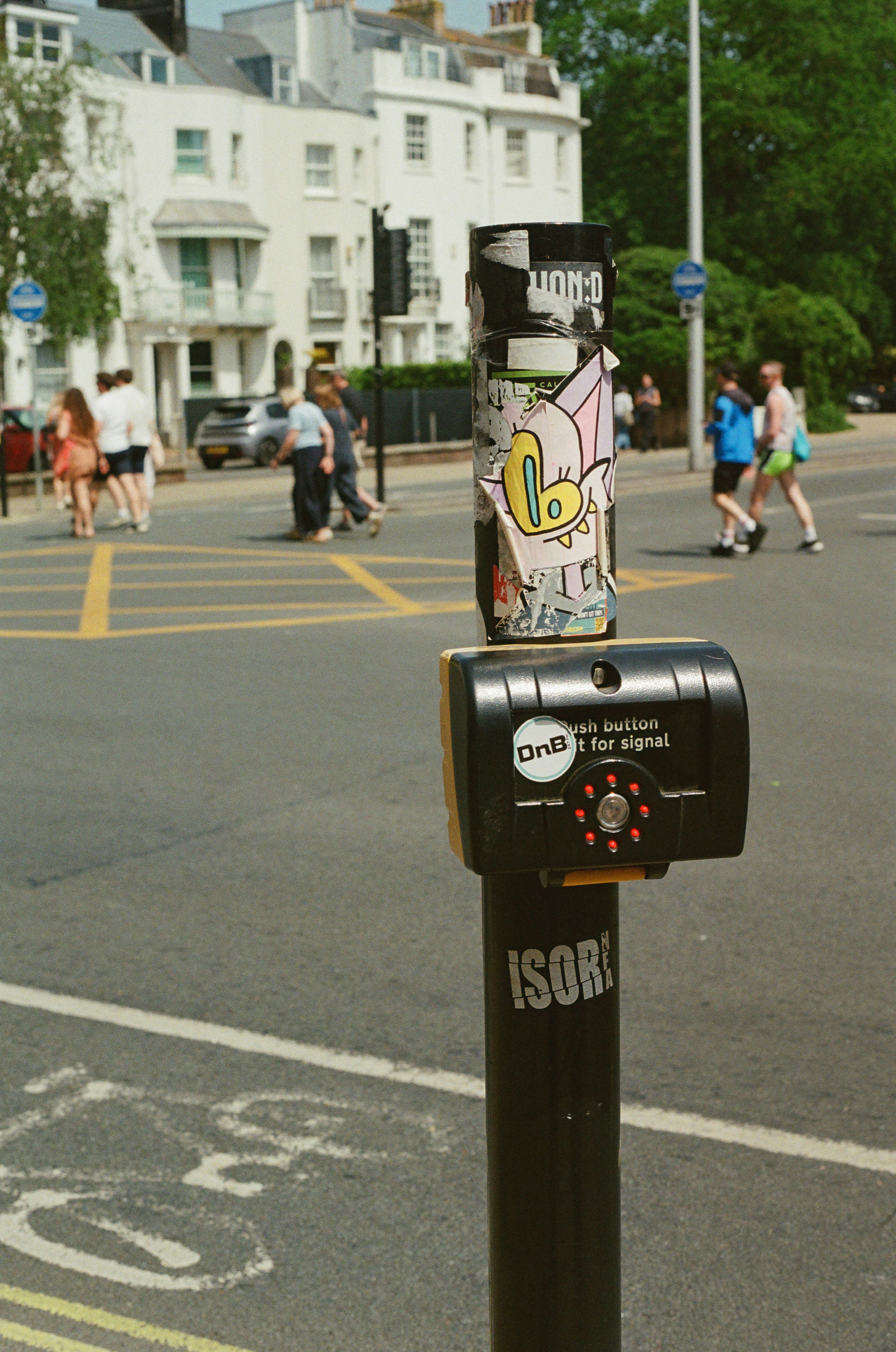 Graffiti-covered pedestrian crossing signal pole on a city street.