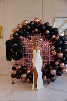 Elegant woman in white dress celebrating 18th birthday with balloons.