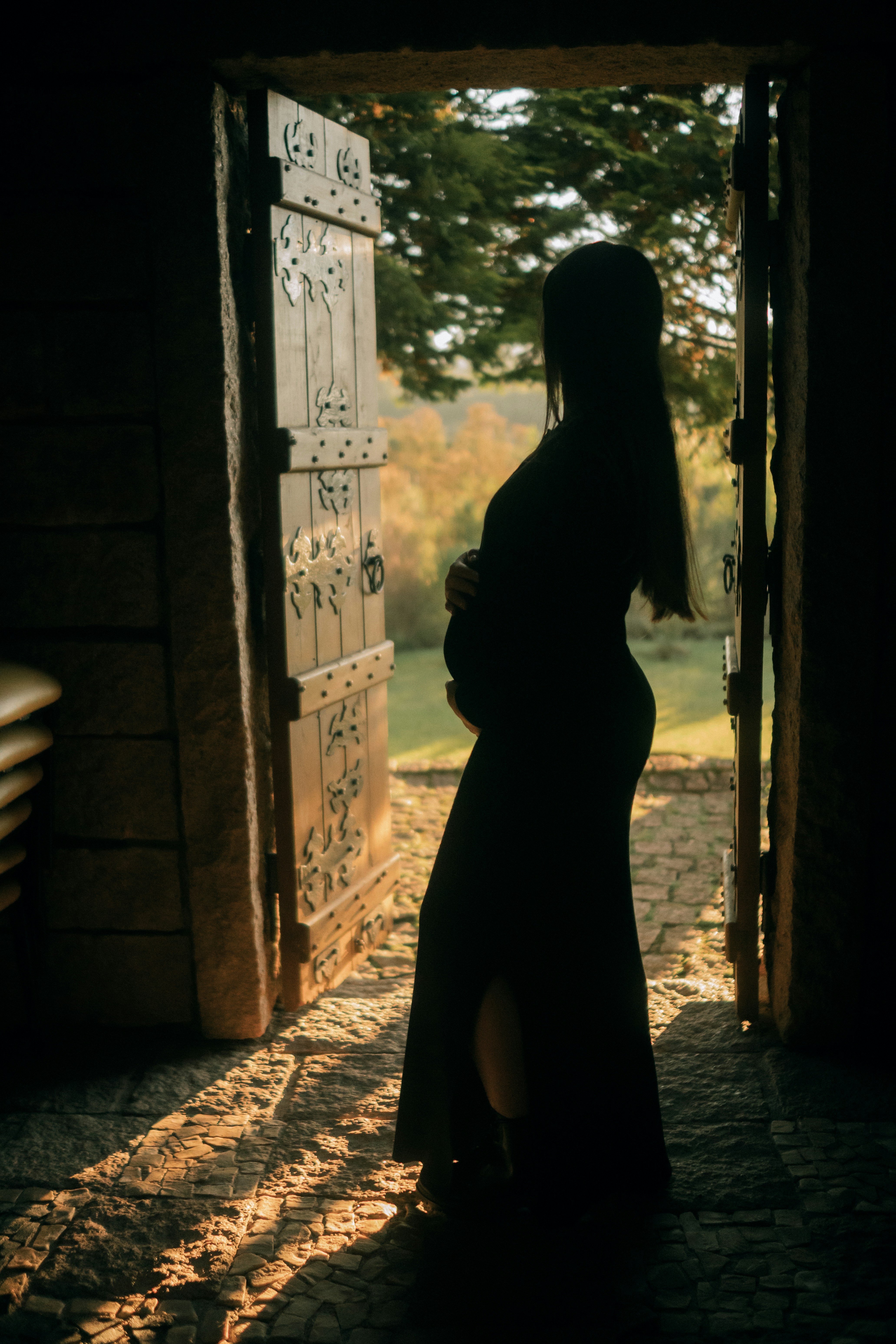 Pregnant woman silhouetted in a rustic doorway at sunset.