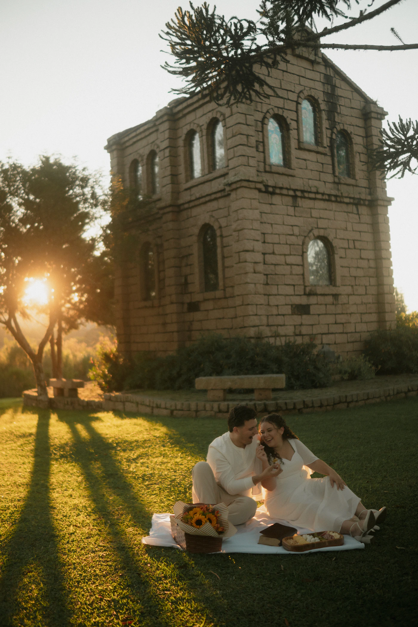 Couple sharing a romantic outdoor picnic near a historic stone building at warm golden sunset