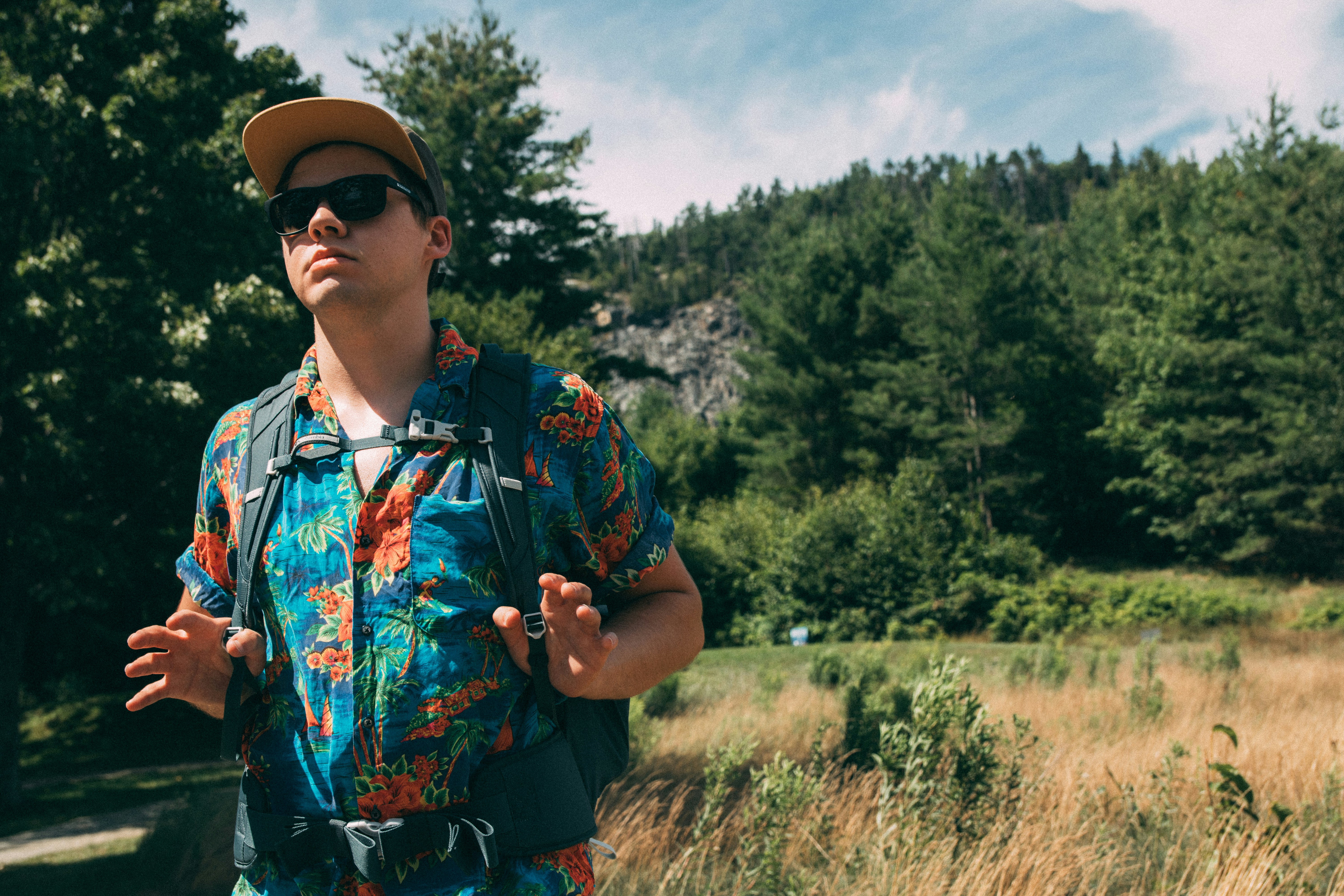 A man in a hawaiian shirt and sunglasses stands outdoors.