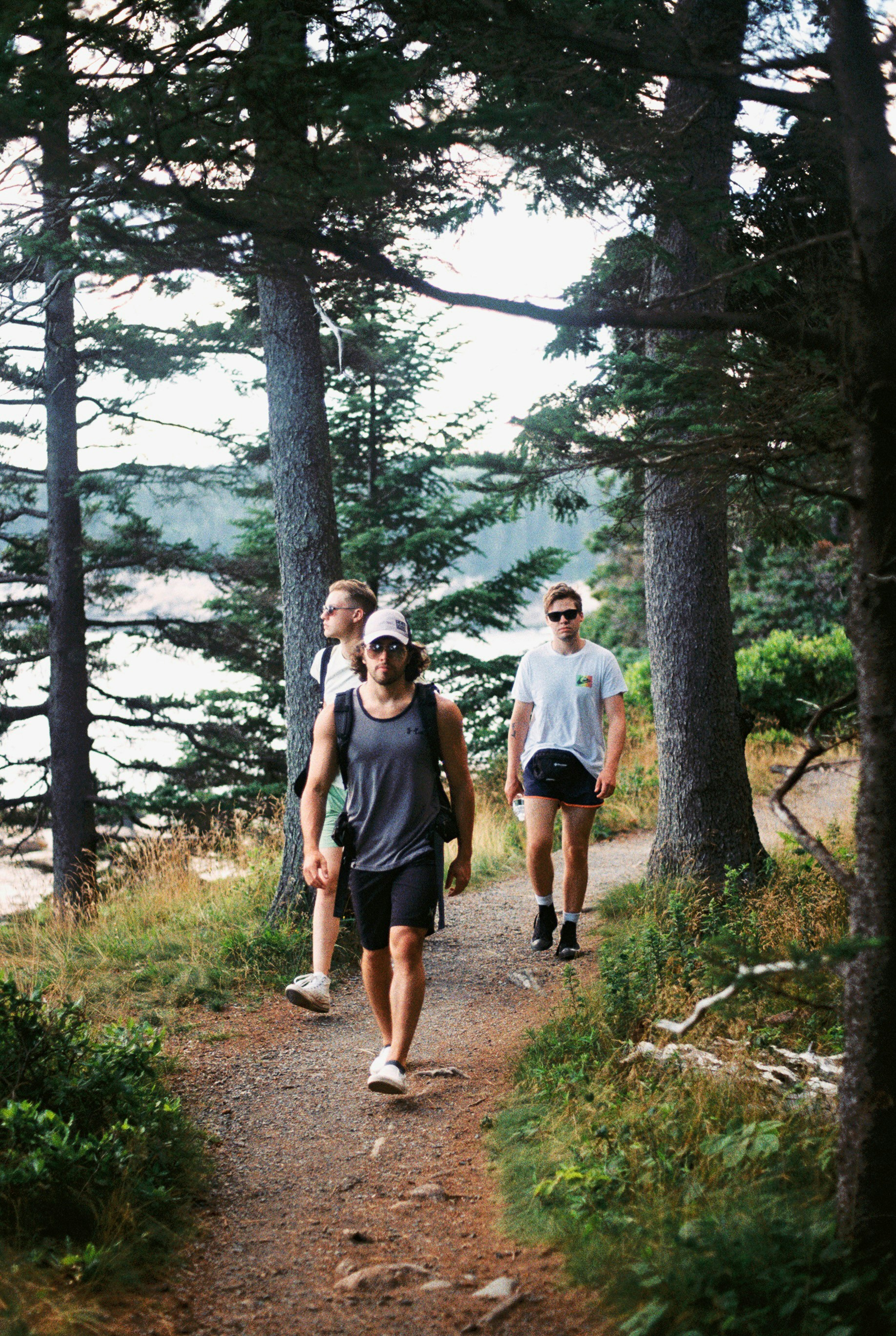 Three men hiking on a forest path near water.