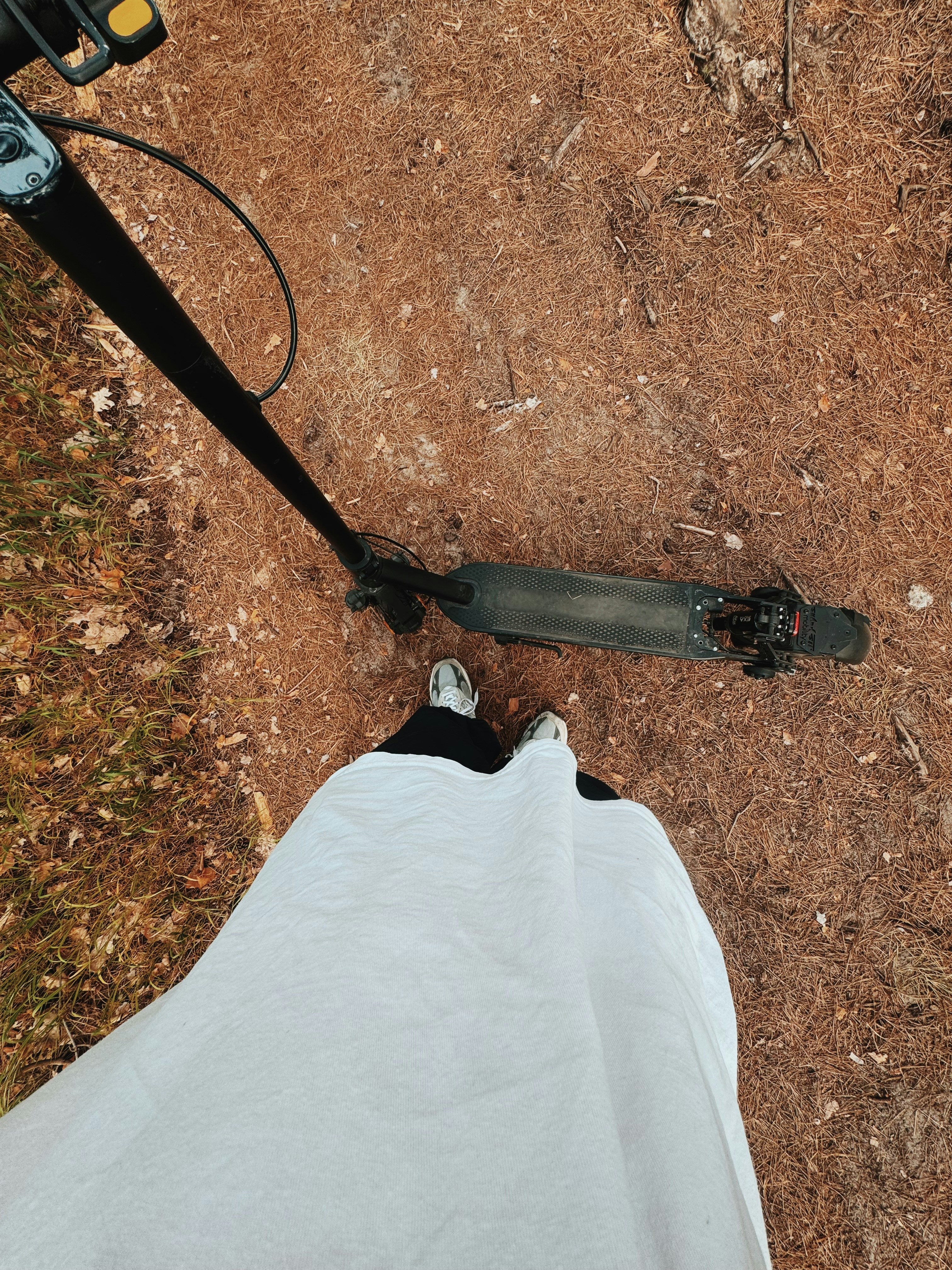 白いスニーカーとスクーターで乾いた葉の道を歩いています。