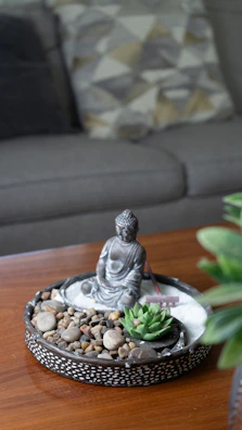 Miniature zen garden with buddha statue on wooden table.