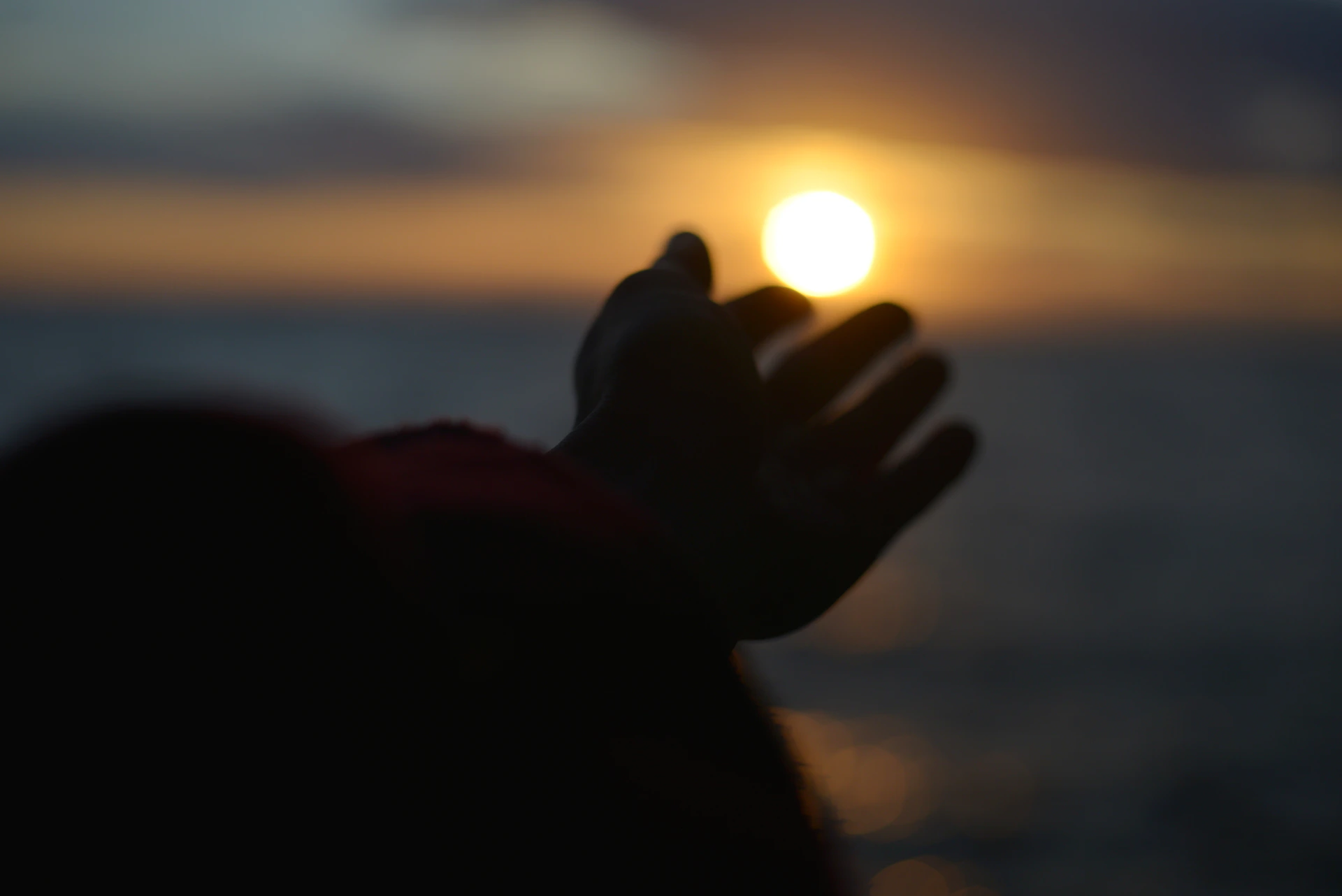 Silhouetted hand reaching for the bright sun over the water