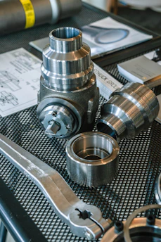 Various metal mechanical parts and blueprints on a mesh table