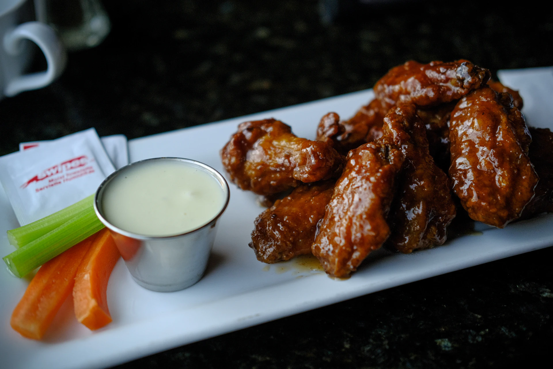 Glazed chicken wings with dipping sauce, celery, and carrots.