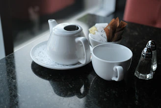 White teapot, teacup, sugar, and shakers on a dark table