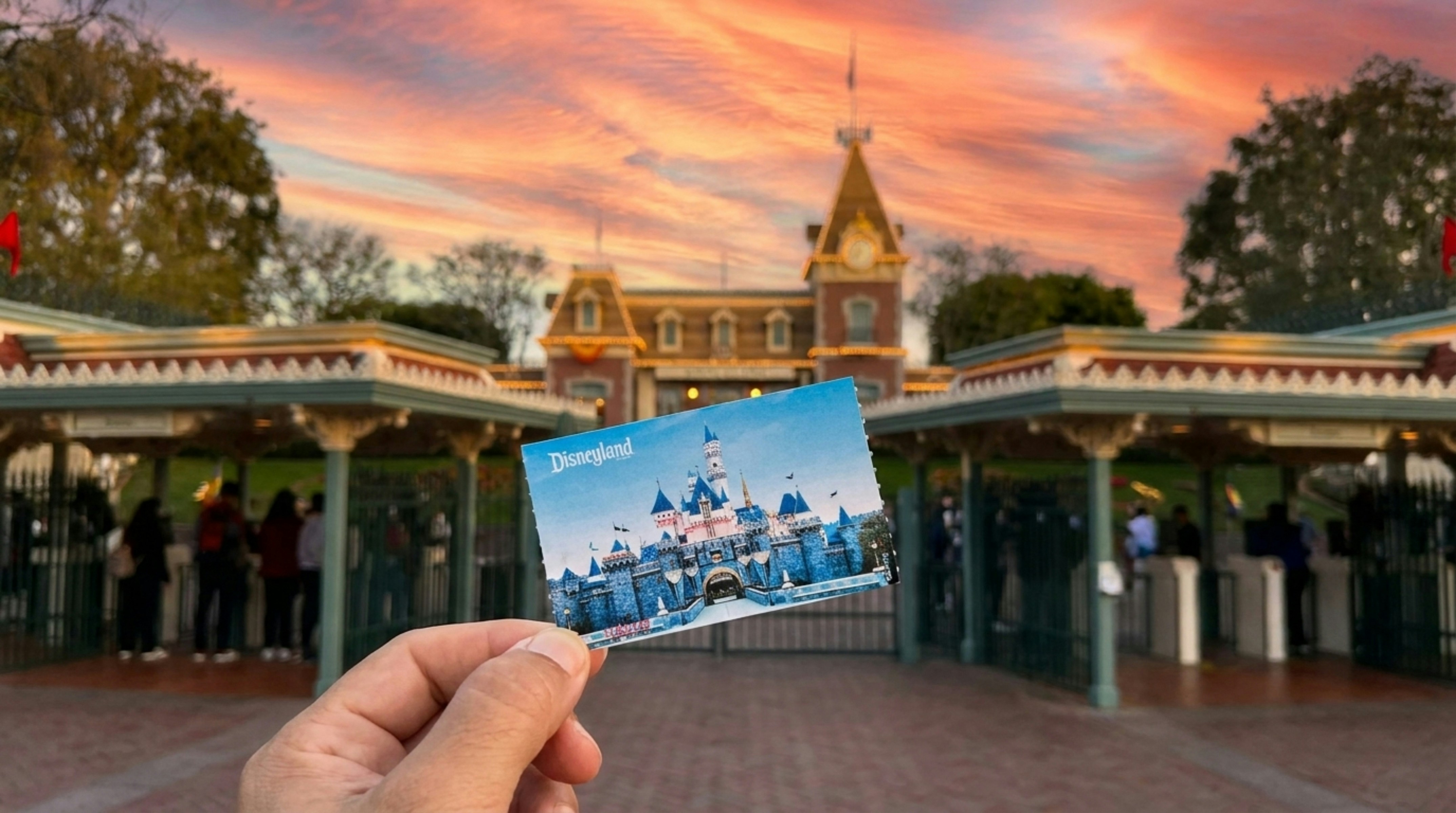 Hand holds disneyland ticket before park entrance at sunset.