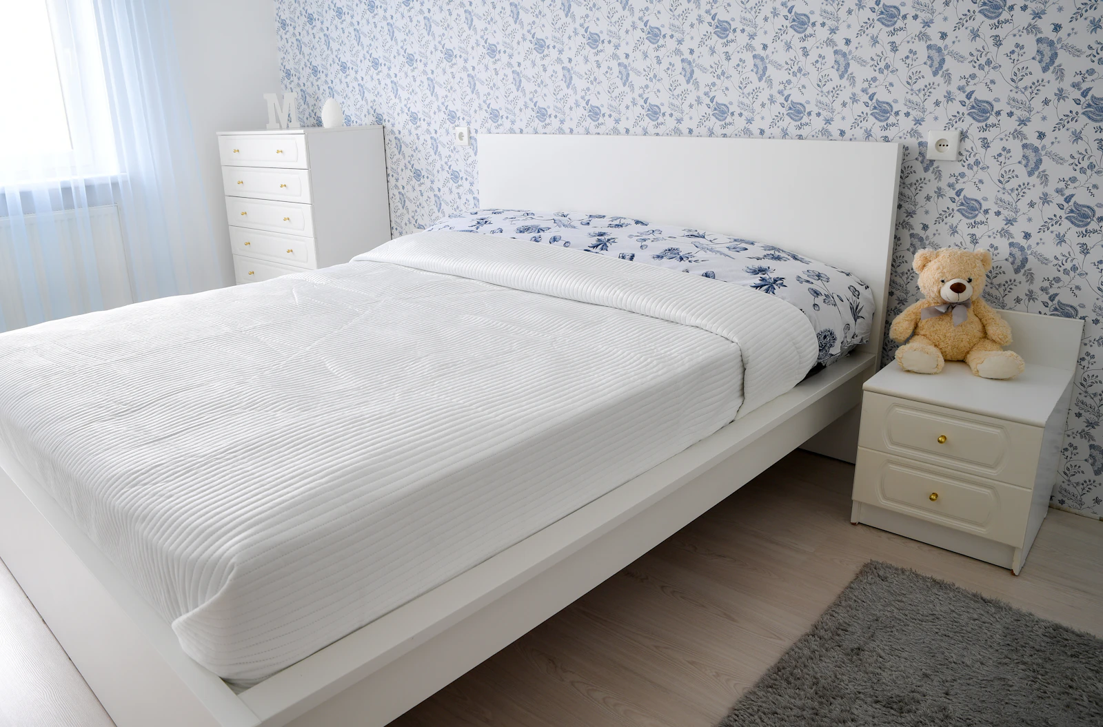 A white bedroom with a bed and a dresser
