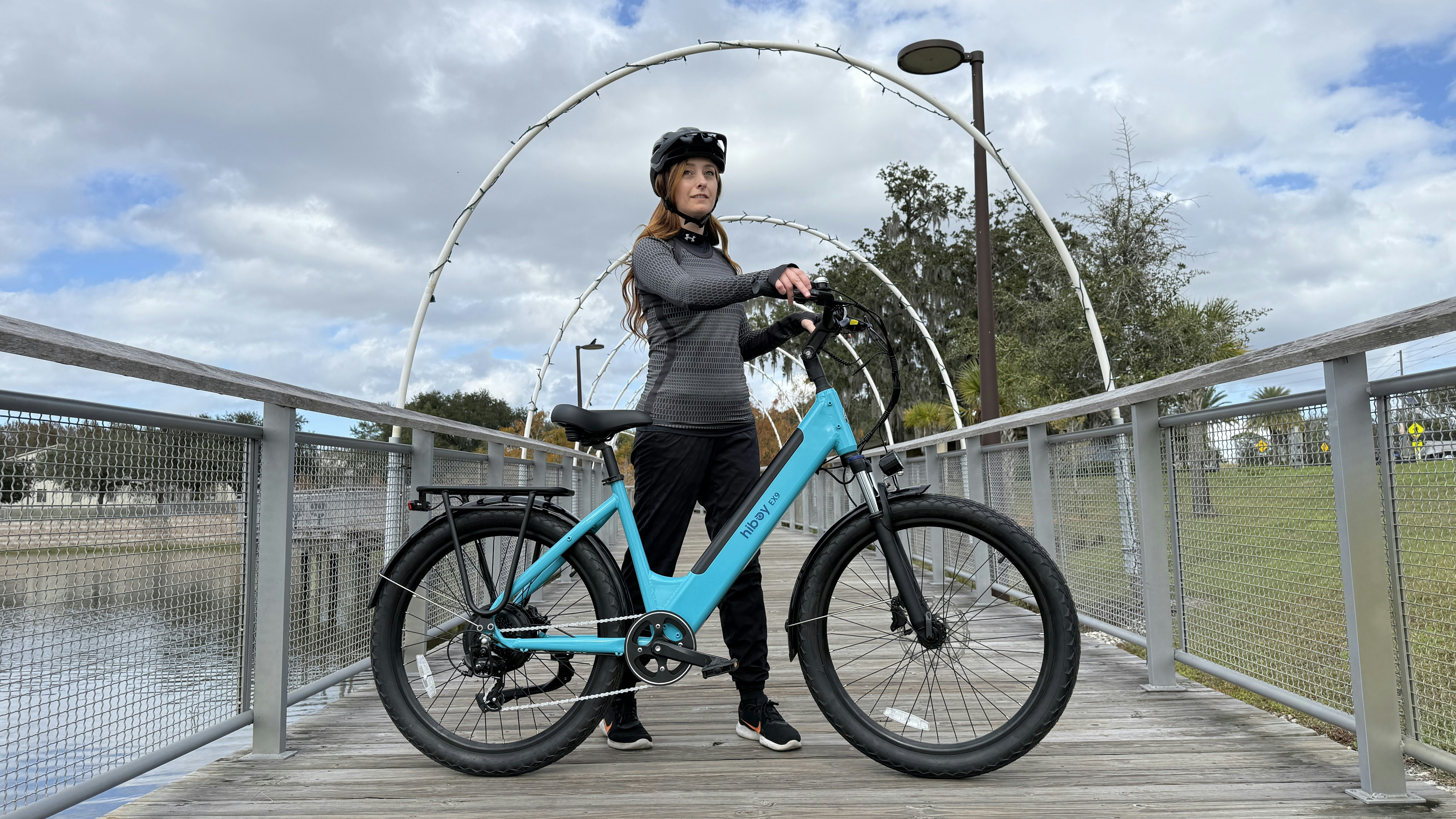 A woman stands with her turquoise bicycle on a bridge