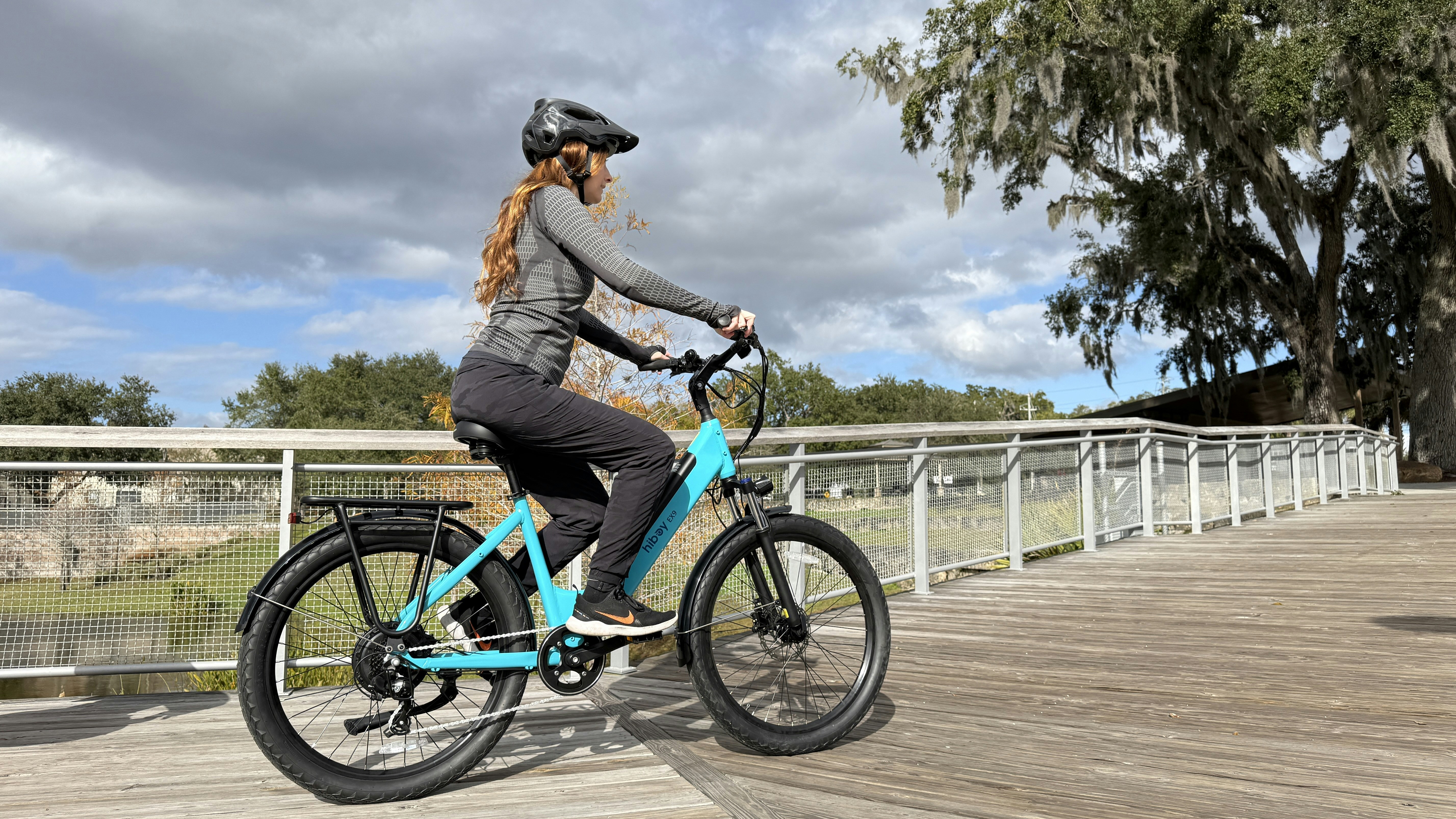 A woman rides a turquoise bicycle on a wooden boardwalk