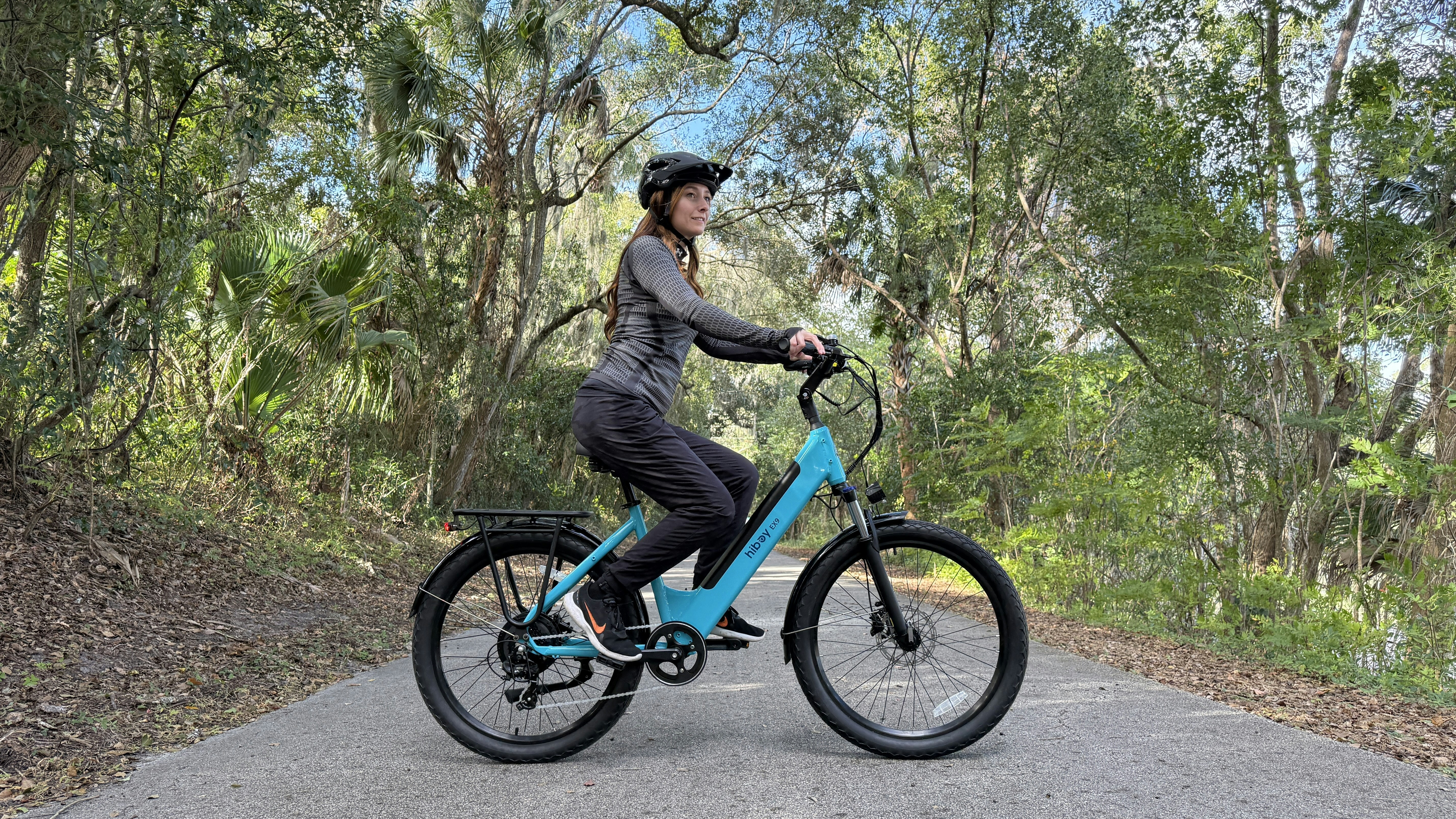 A woman rides a blue bicycle on a park path