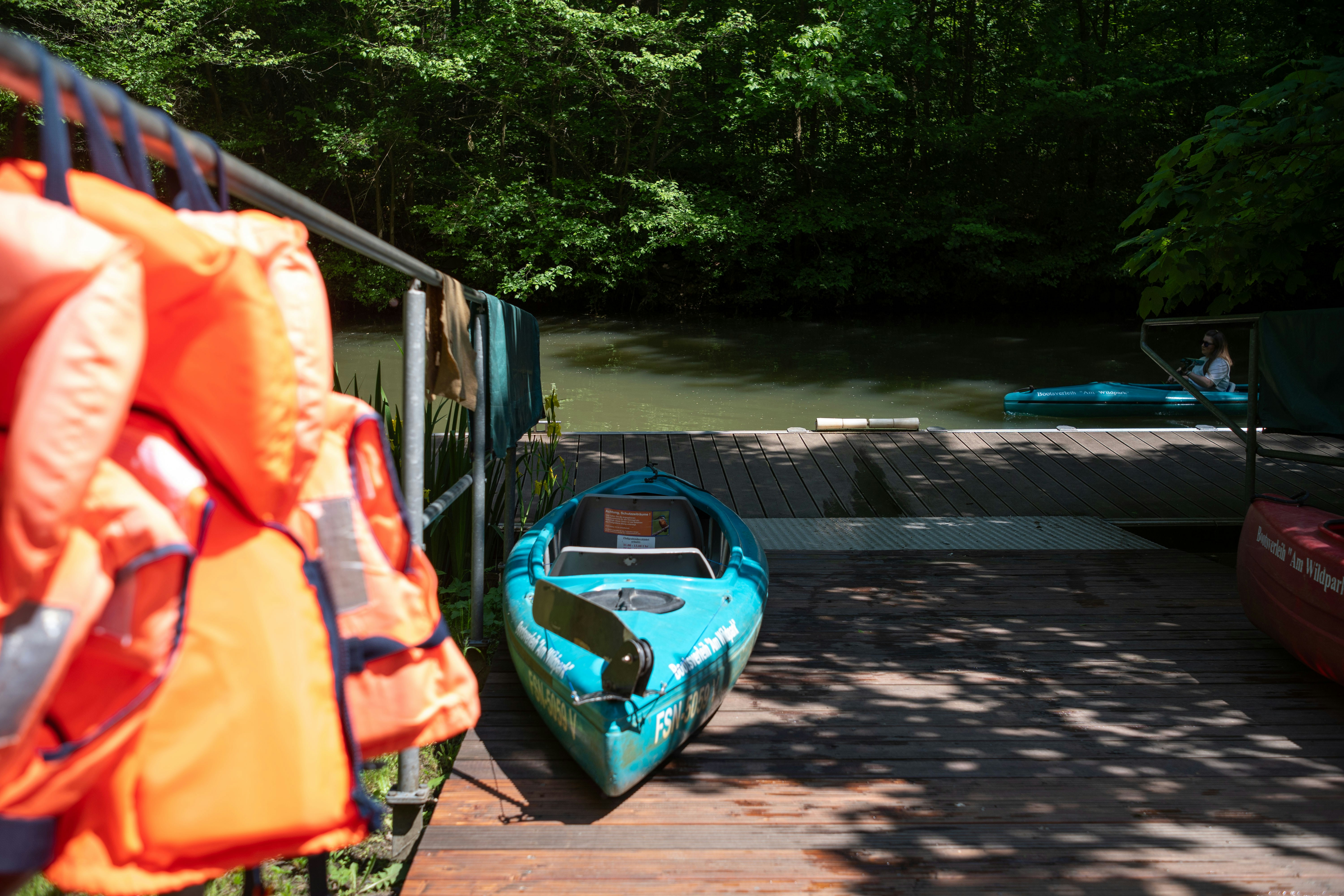 Orange life jackets and blue kayak on dock near river.