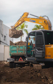 Yellow excavator moving soil into a dump truck.