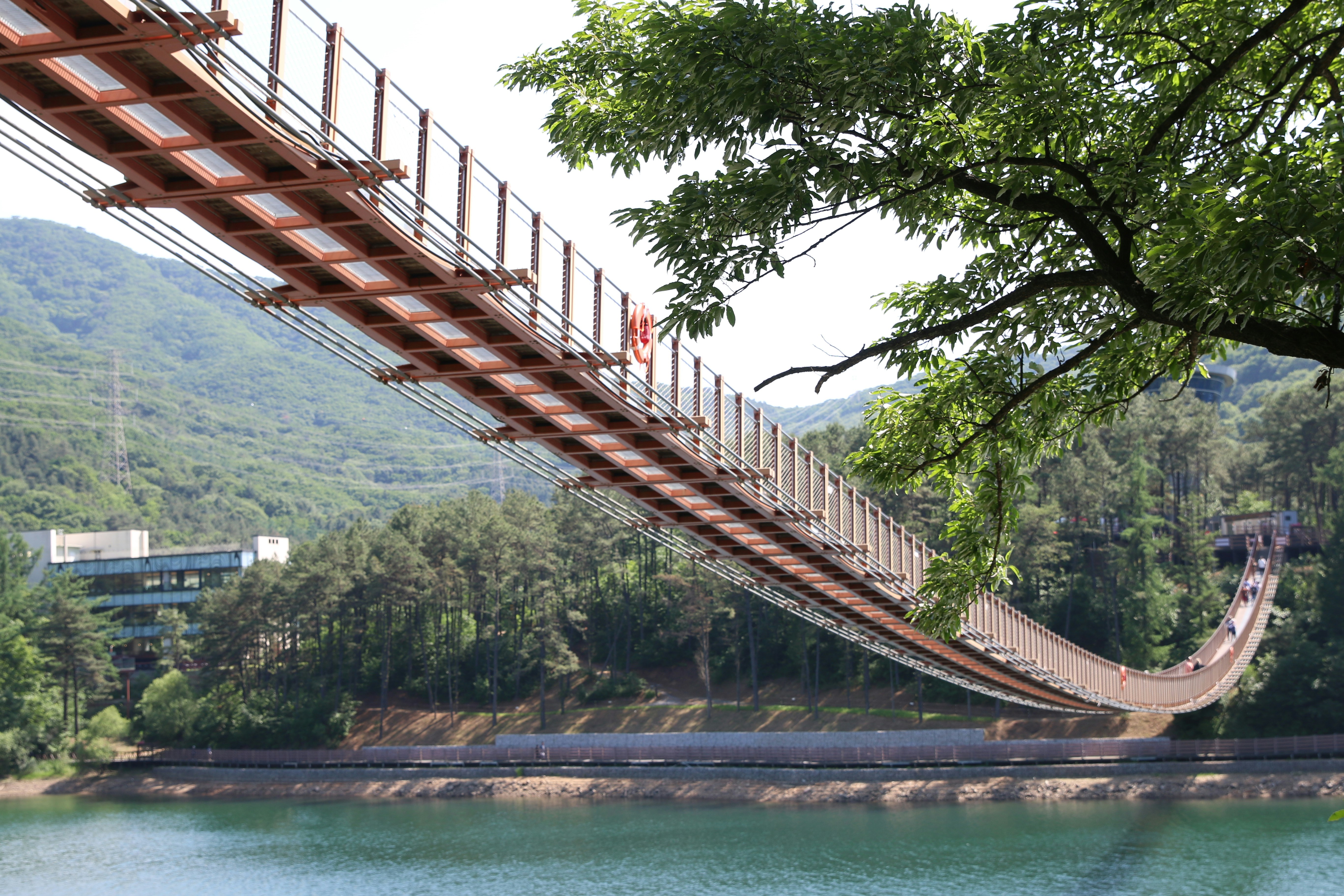 A suspension bridge spans a lake surrounded by green mountains