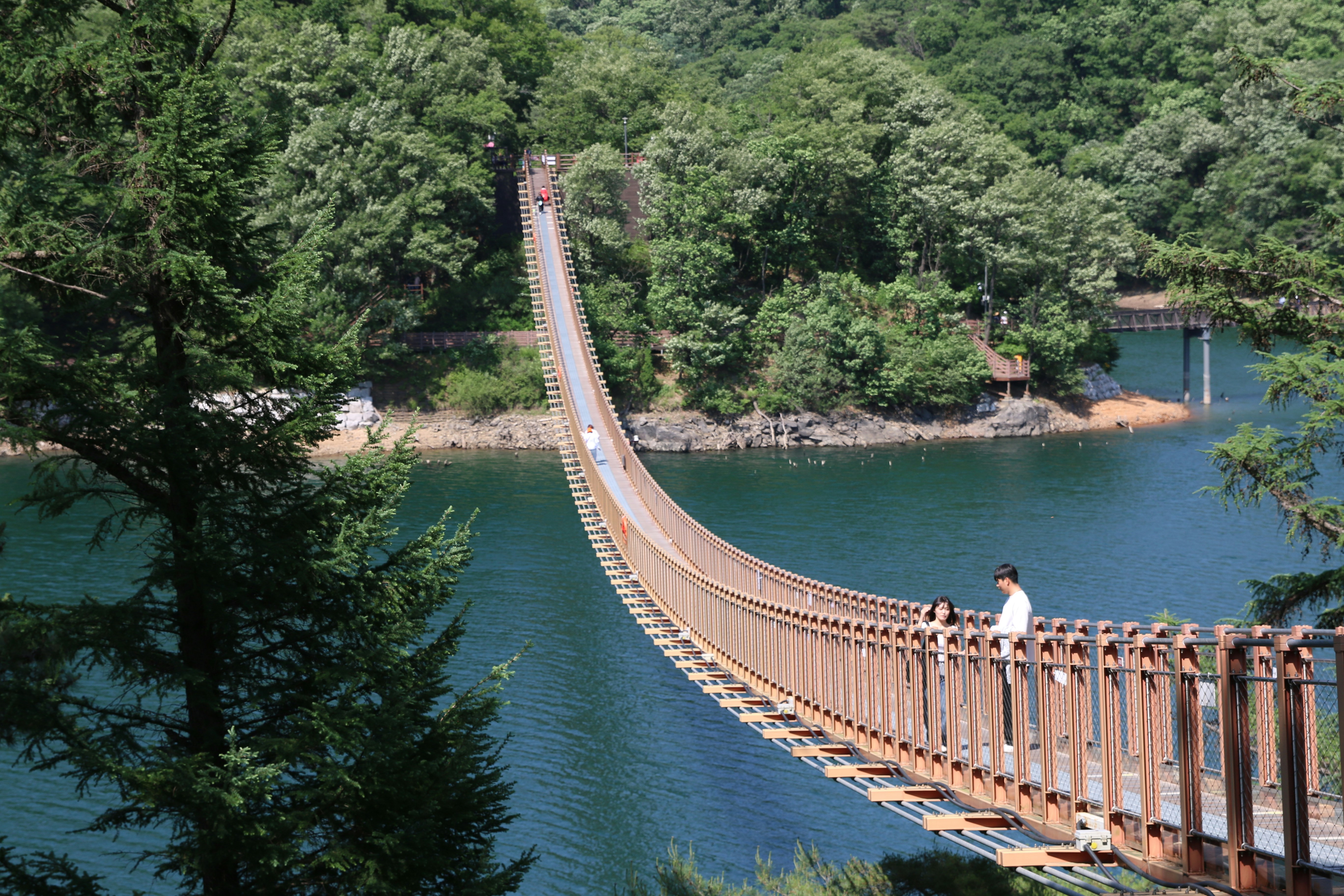 Person crosses a long suspension bridge over a blue lake