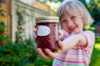 A smiling child holds out a jar of homemade jam.