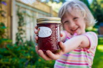 A smiling child holds out a jar of homemade jam.
