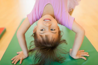 A young girl smiling upside down on a green mat