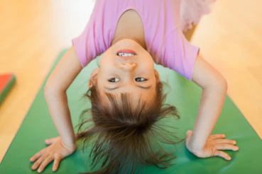 A young girl smiling upside down on a green mat