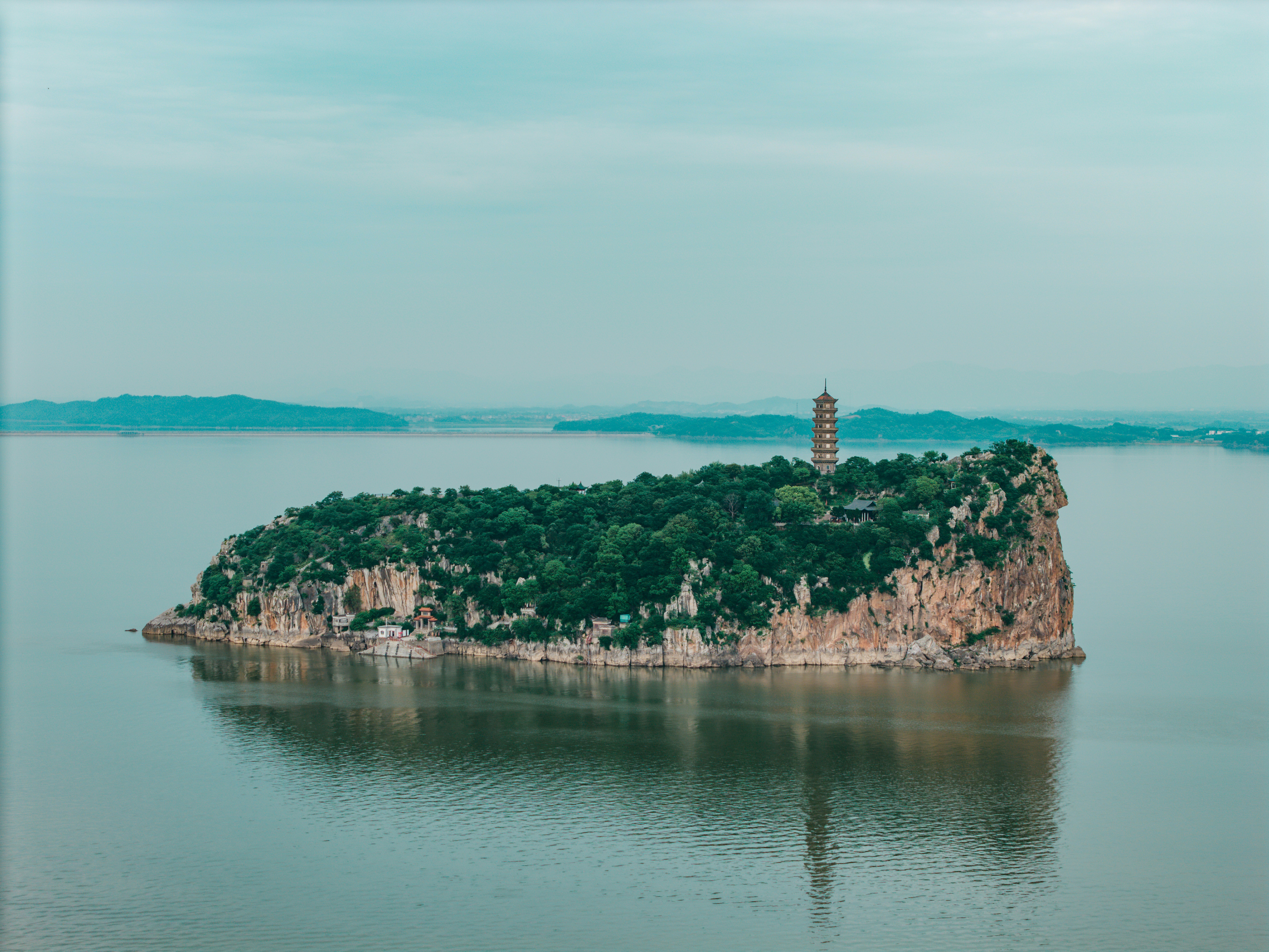 Pagode auf einer felsigen, bewaldeten Insel in ruhigem Wasser.