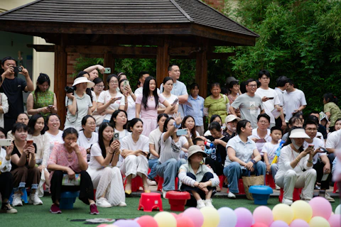 People watching an outdoor event, colorful balloons in foreground.