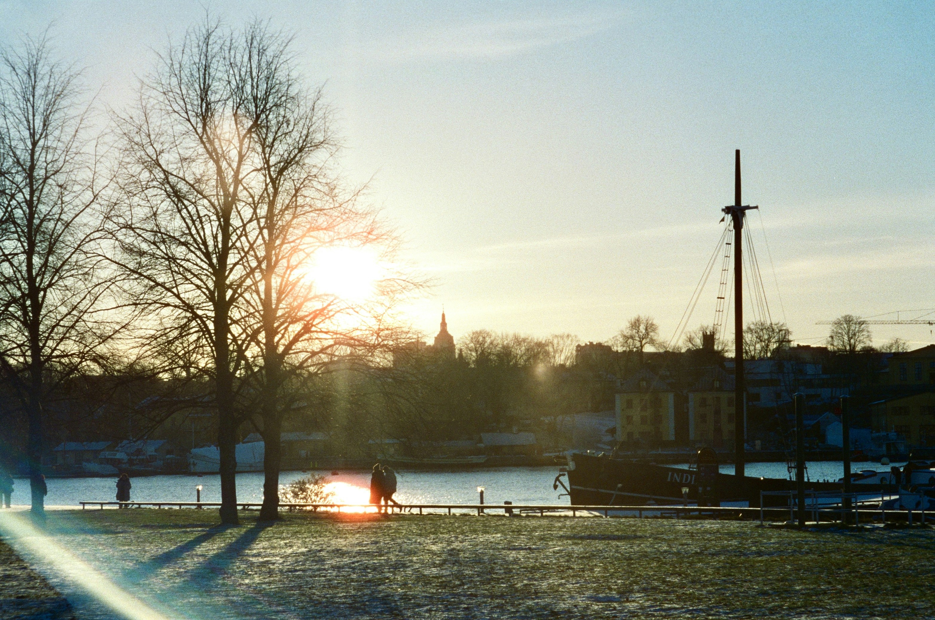 Sunset over a waterfront with trees, people, and a boat