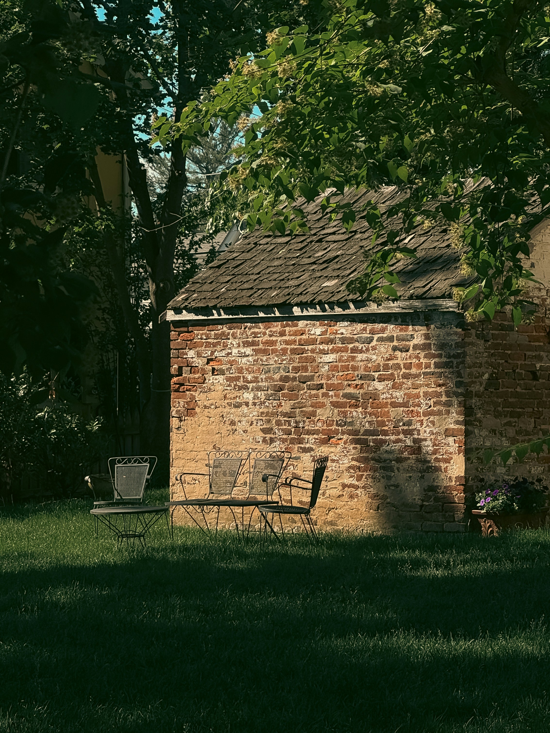 Old brick building with two chairs in a grassy yard.