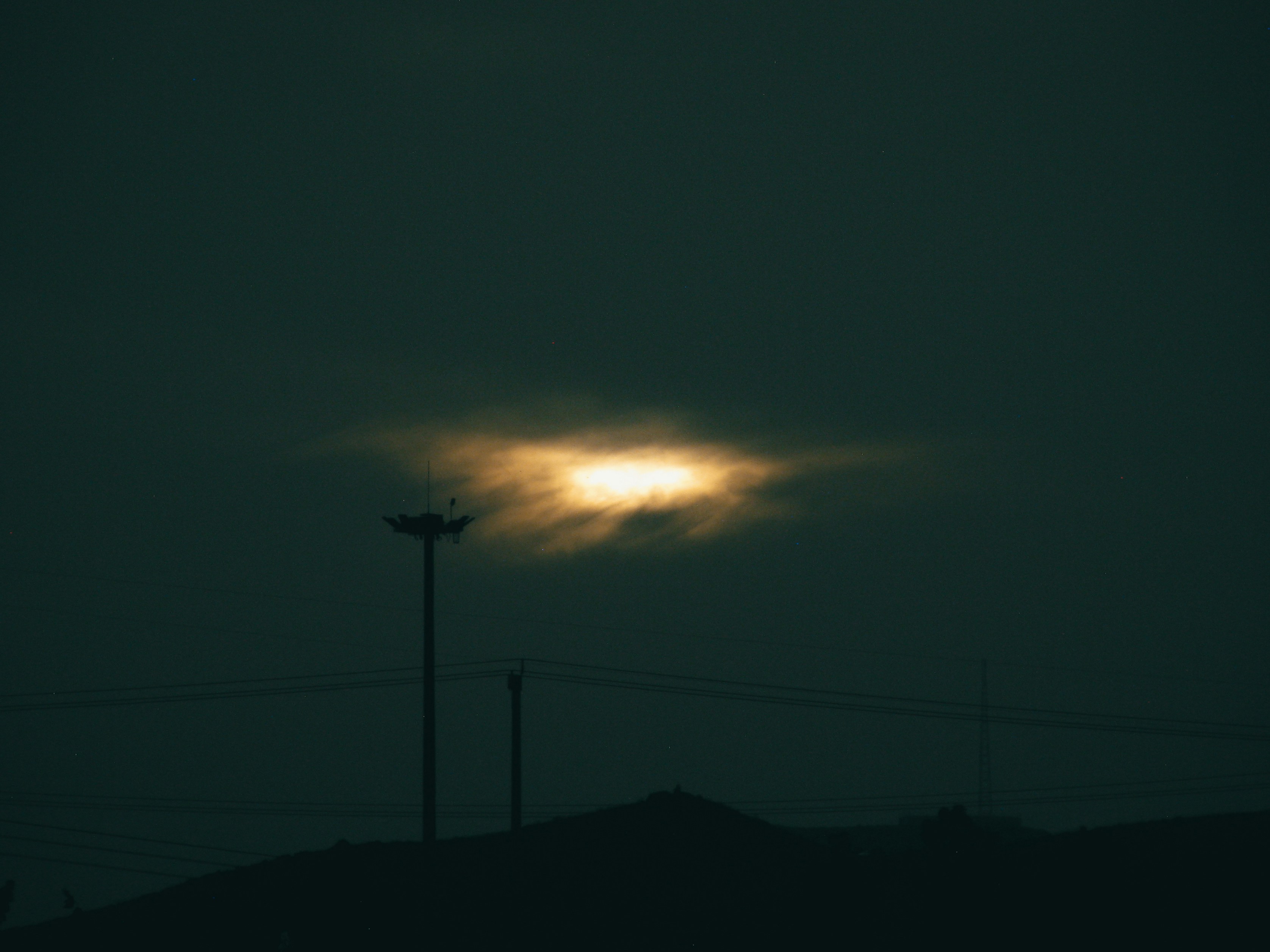 Dramatic dark sky with glowing sun behind silhouetted poles.