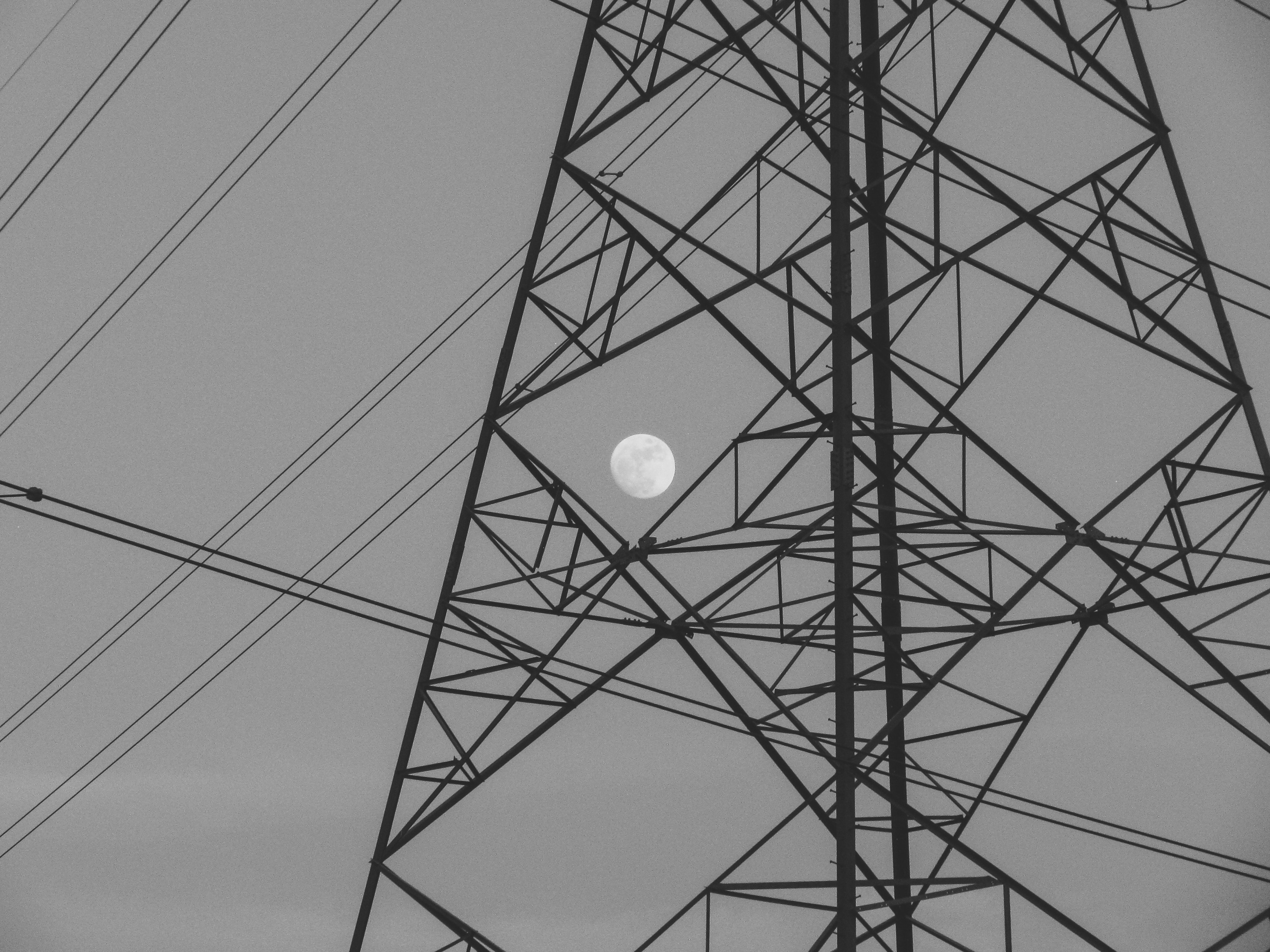 Full moon visible through a large power line pylon.