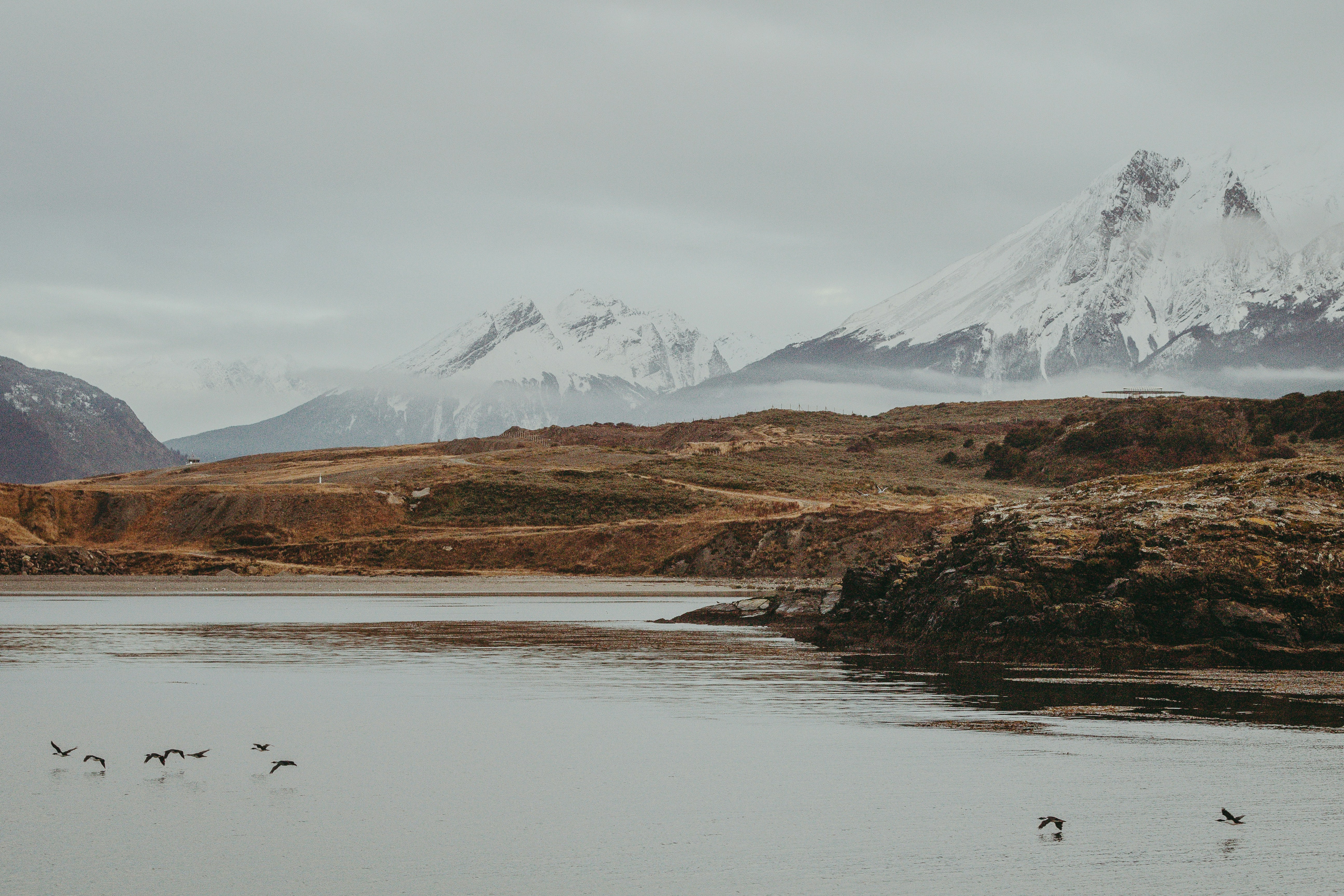 Snow-capped mountains overlook a calm lake with rocky shores