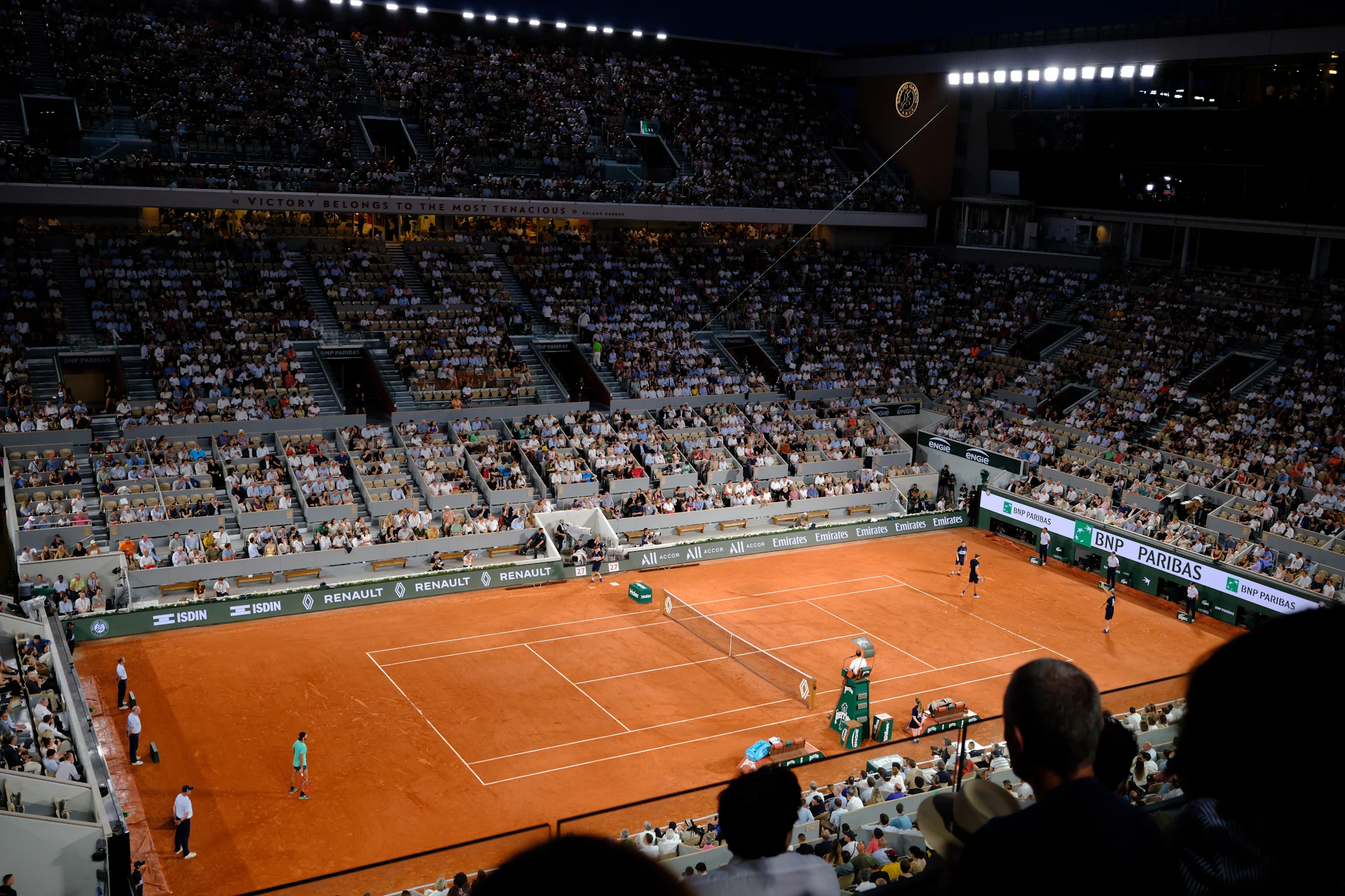 A crowded tennis stadium with a clay court at night