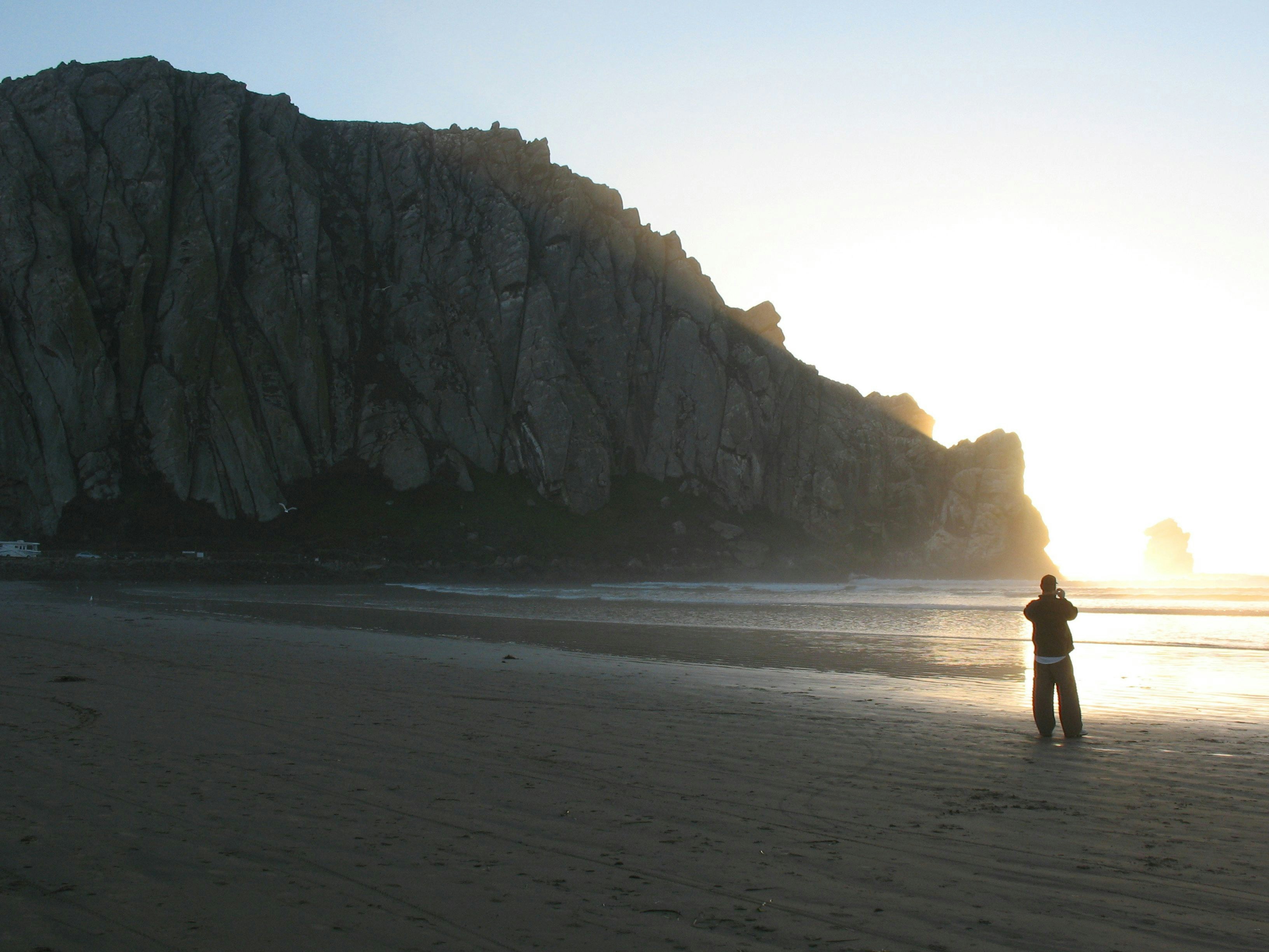 Person on beach at sunset near large rock.