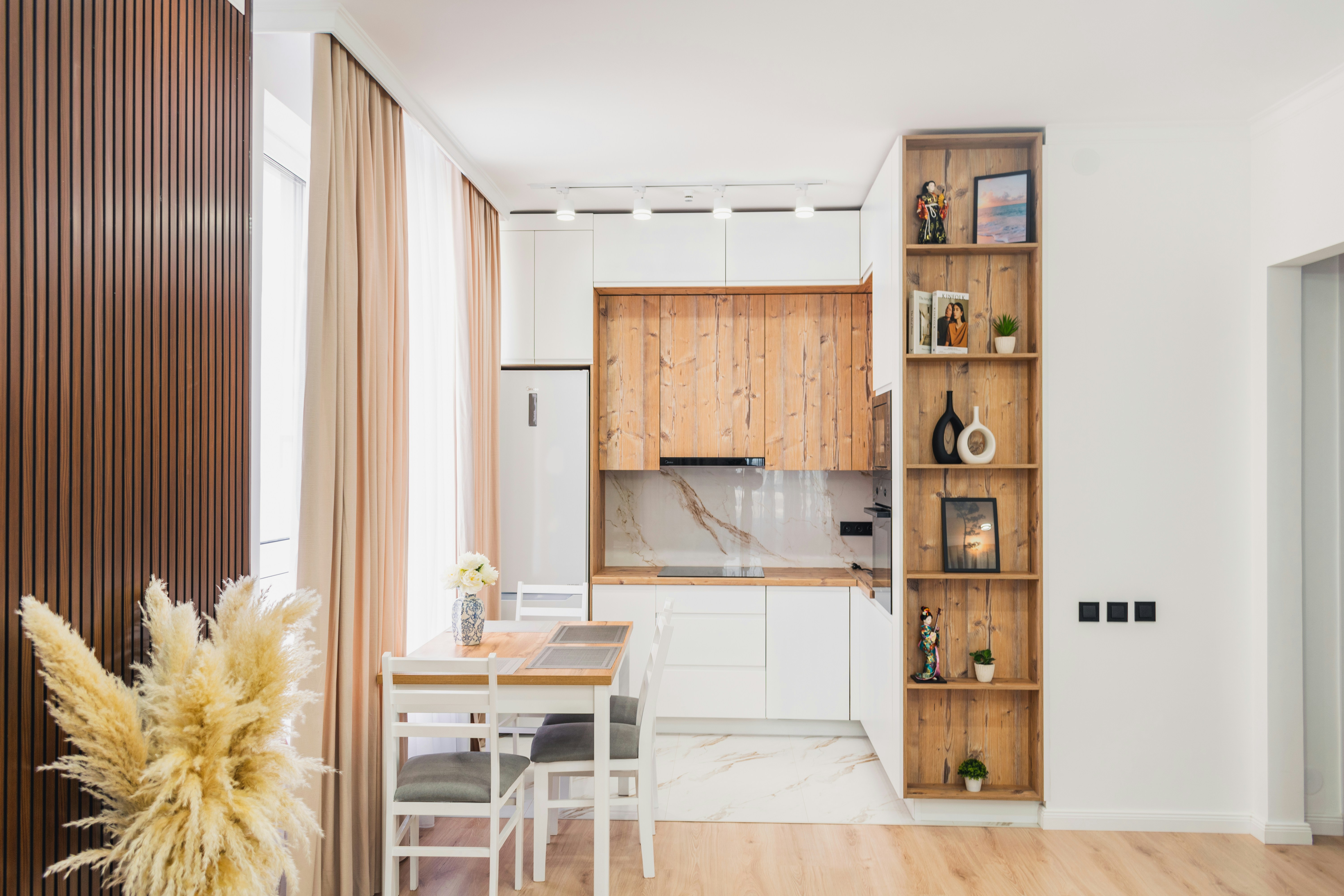 Compact modern apartment dining area with warm wood-toned drop-leaf table and matching wooden kitchen cabinets