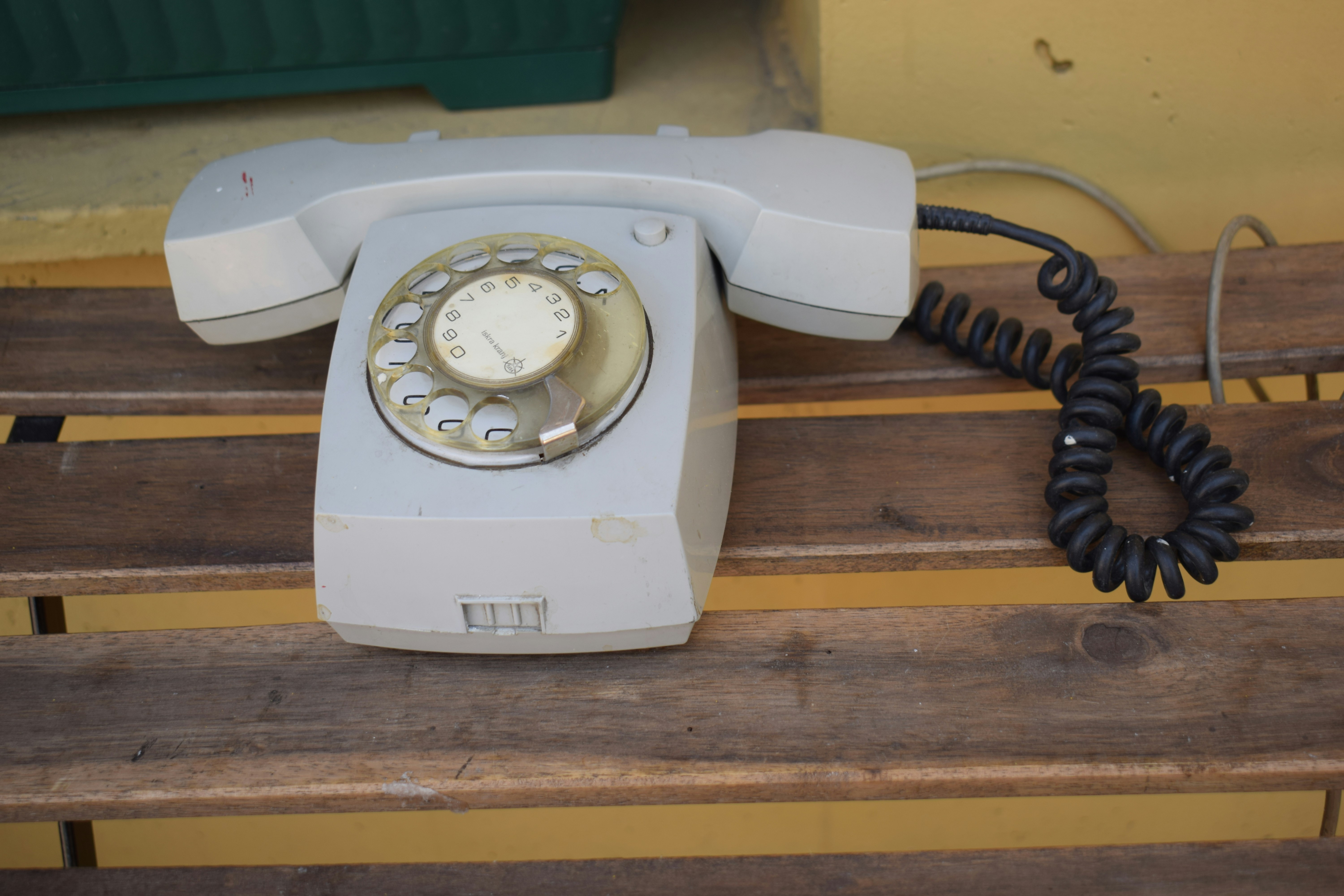 Un viejo teléfono rotatorio gris descansa sobre un banco de madera.